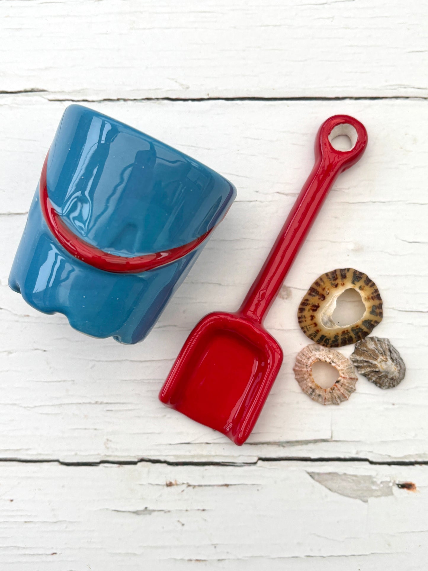 blue ceramic bucket with red stripe, matching spoon, and seashells—playful coastal decor for beach-themed breakfast styling