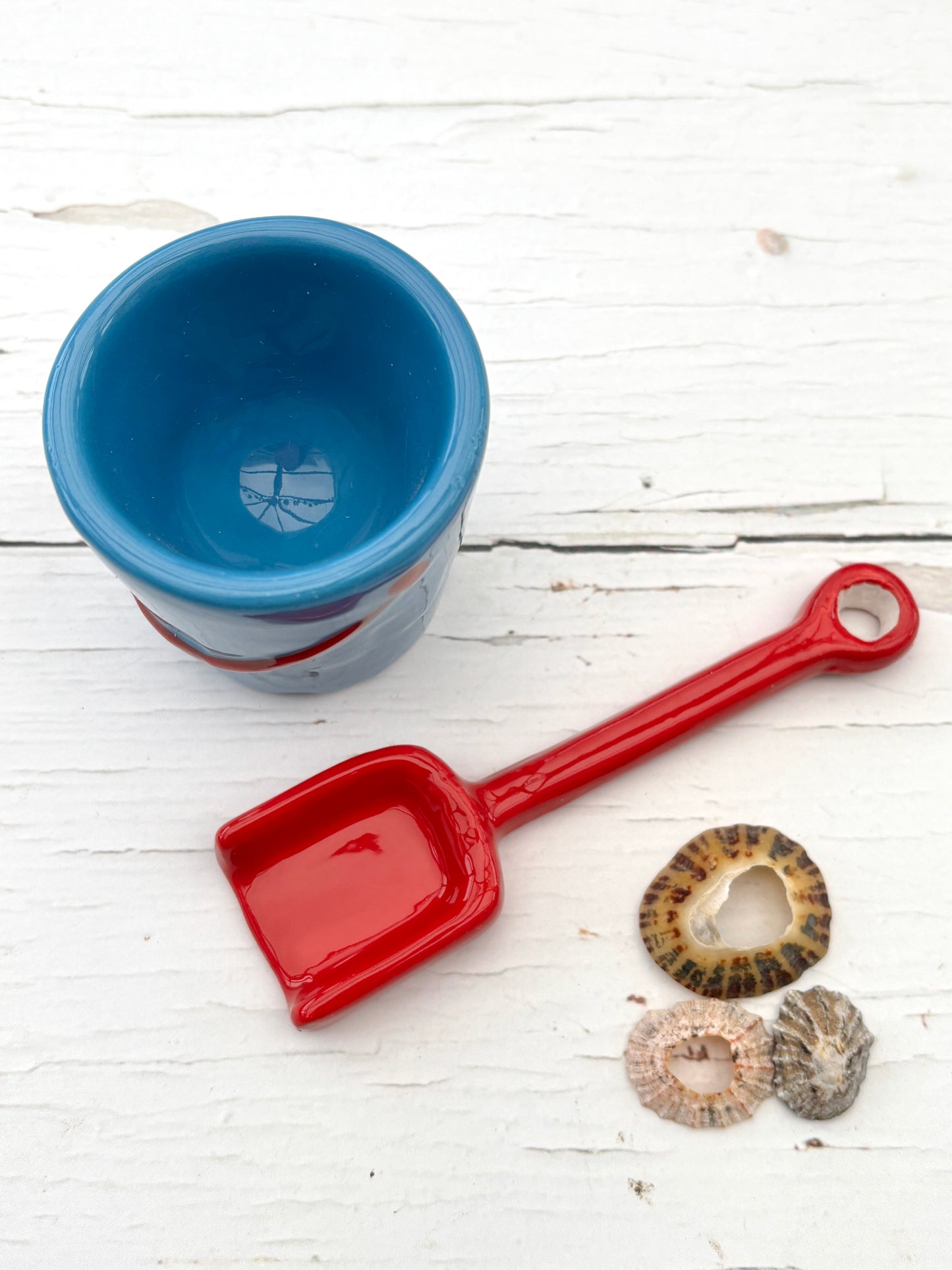 striped ceramic egg cup with red spoon and seashells—playful beach-themed decor for coastal kitchen styling