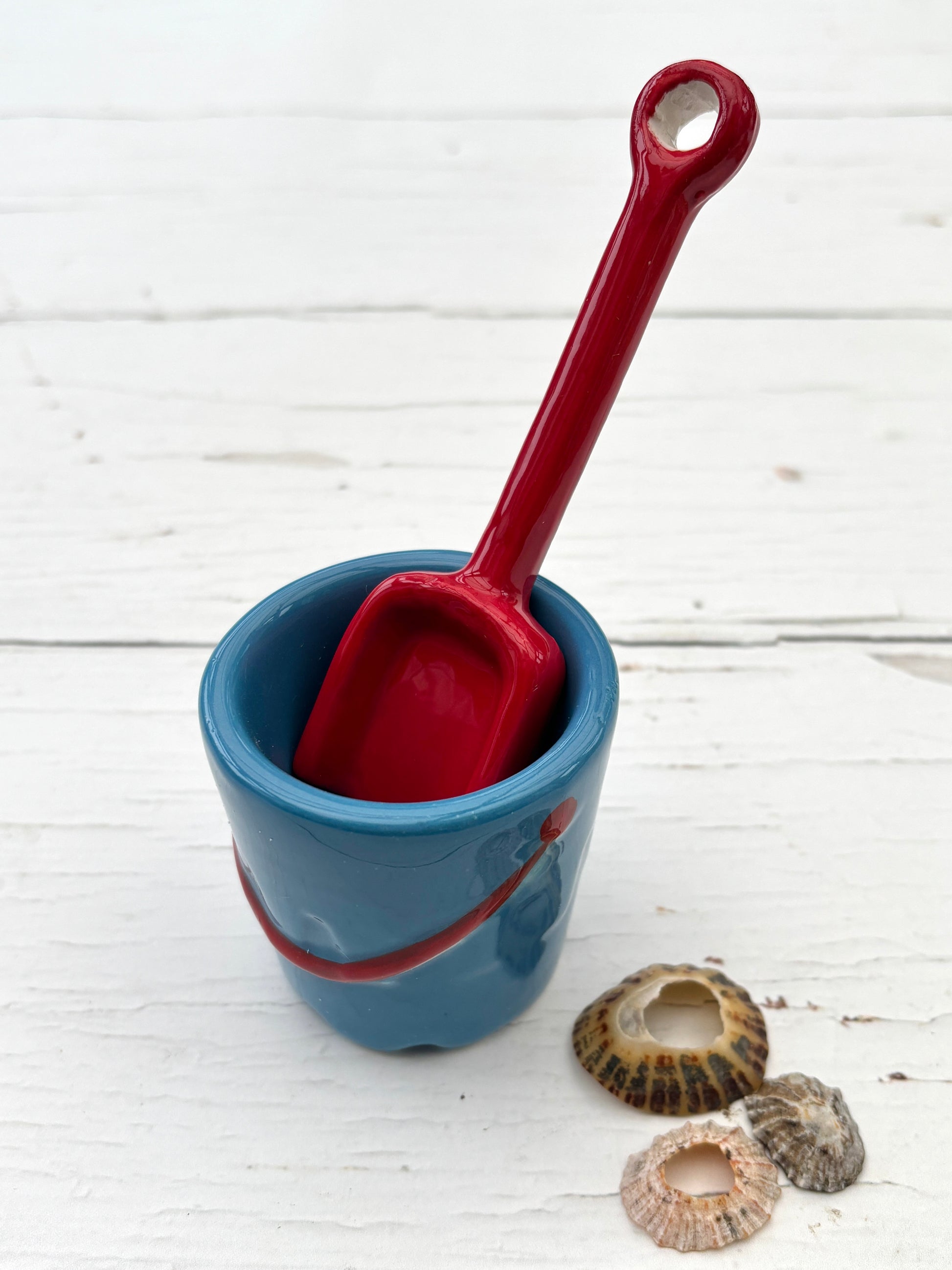ceramic beach bucket egg cup with red shovel and seashells—fun coastal kitchen accent for seaside-inspired styling