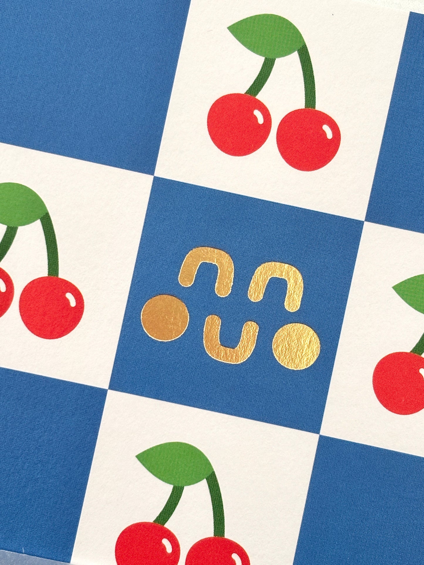 closeup shot of Studio Boketto notebook cover blue checkered pattern with red cherries and gold foil logo cute stationery, vibrant design