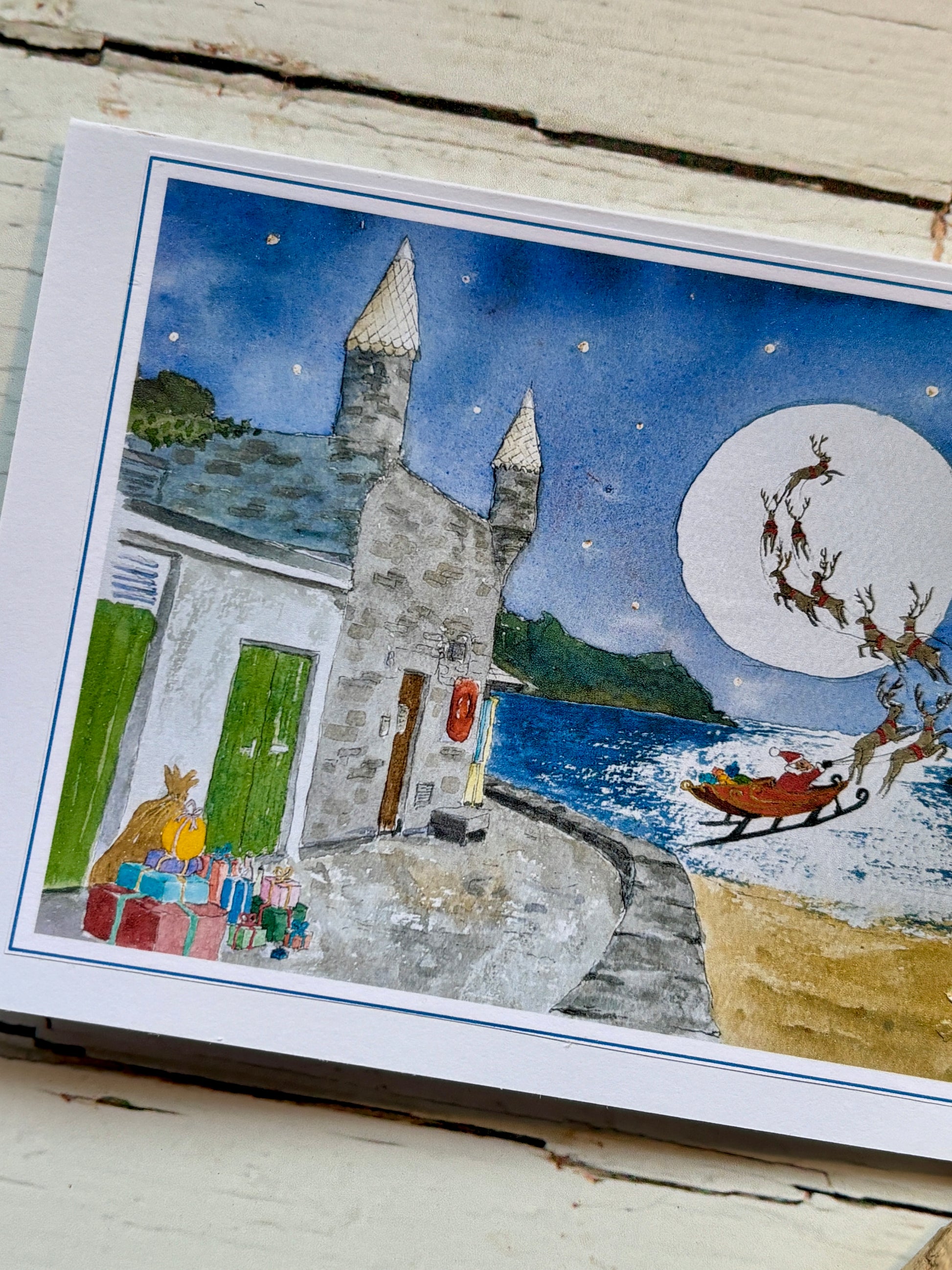 closeup shot of Readymoney Cove Christmas card with watercolour art Santa's sleigh, castle, gifts, seaside holiday greeting card