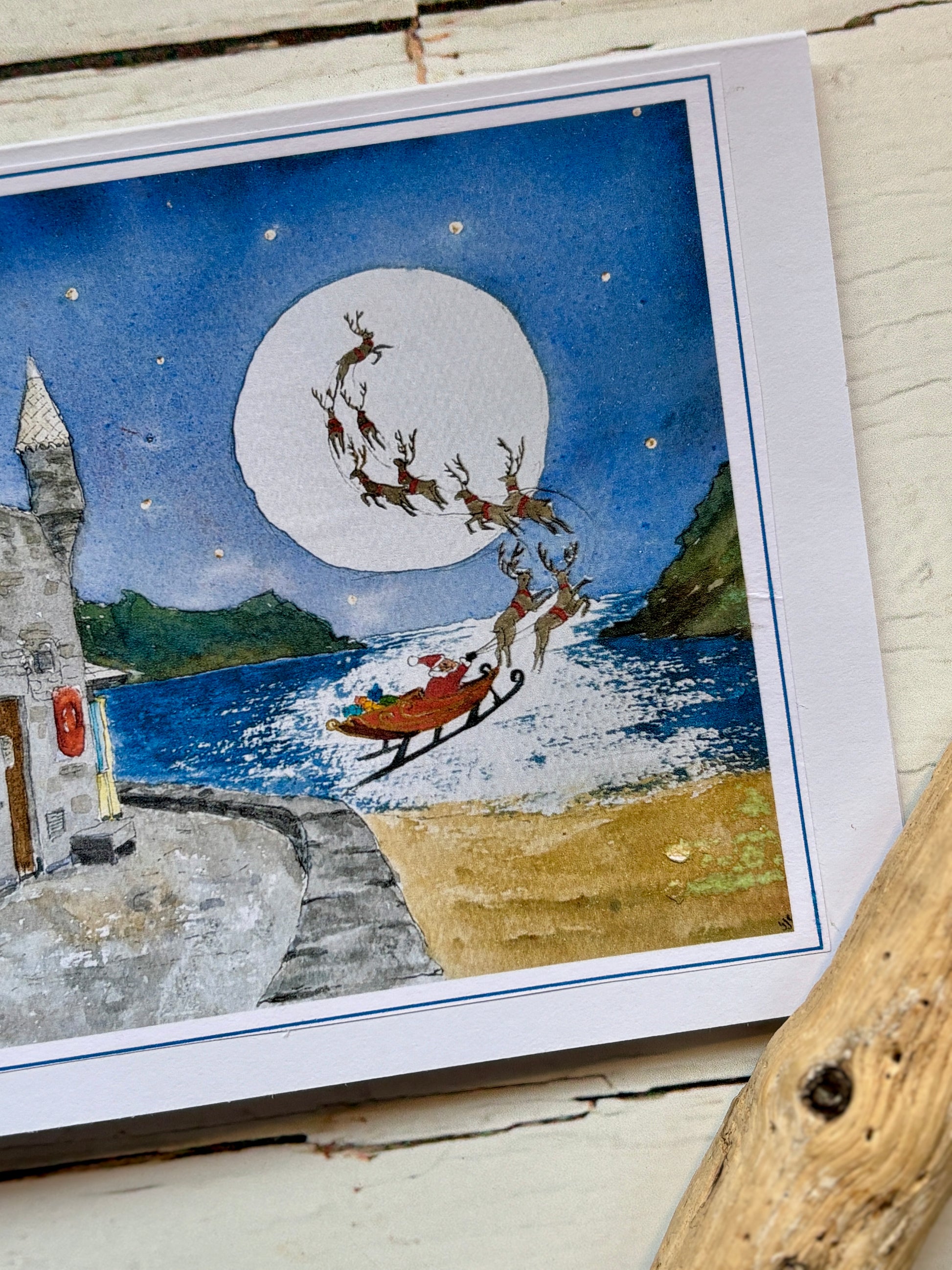 closeup shot of watercolor Christmas card Santa, reindeer, and sleigh flying over Readymoney Beach under a full moon seaside holiday greeting