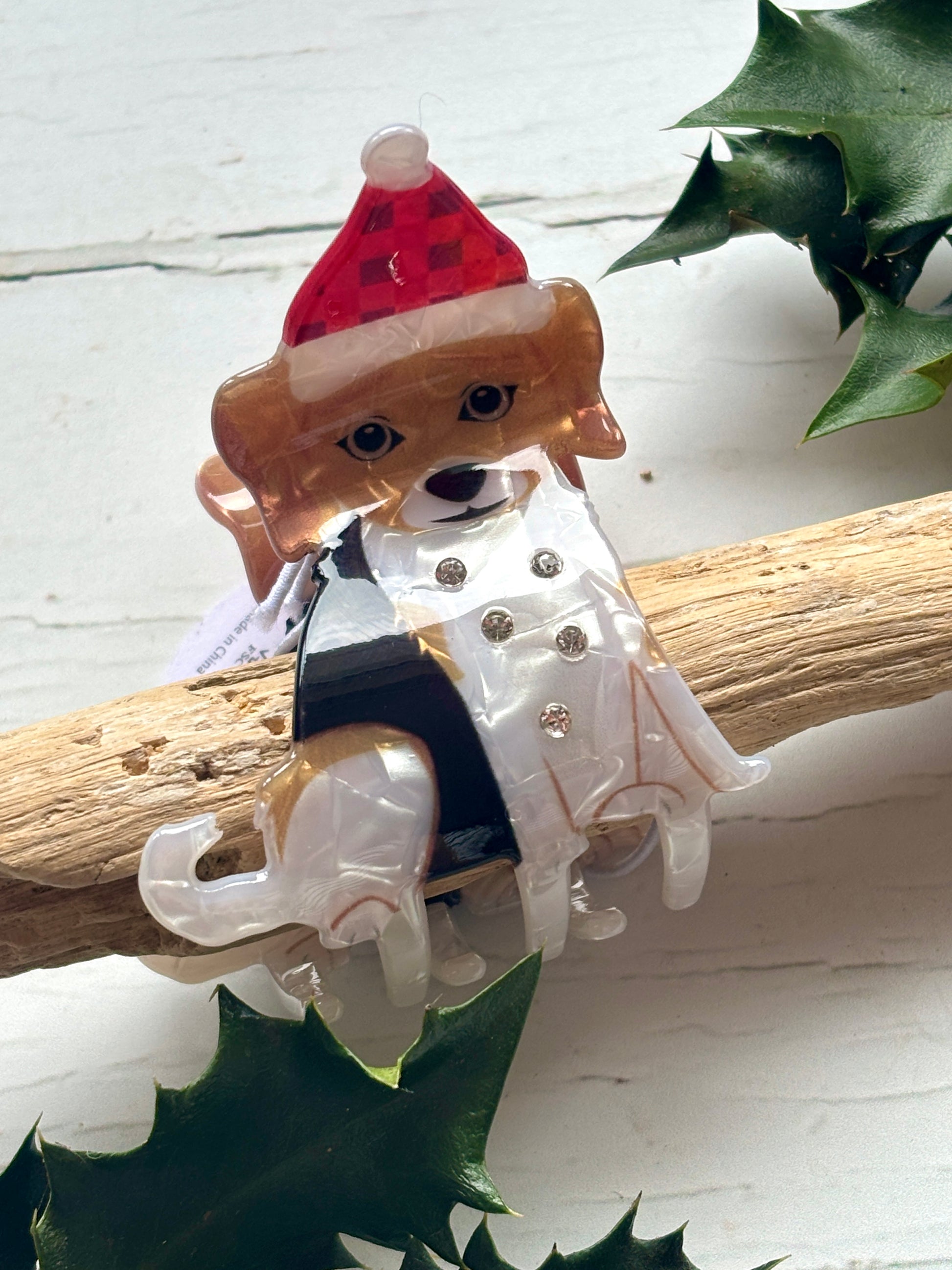 Closeup shot of a festive beagle hair claw clip on a driftwood branch with a plaid Santa hat and sparkly white coat novelty holiday pet gift