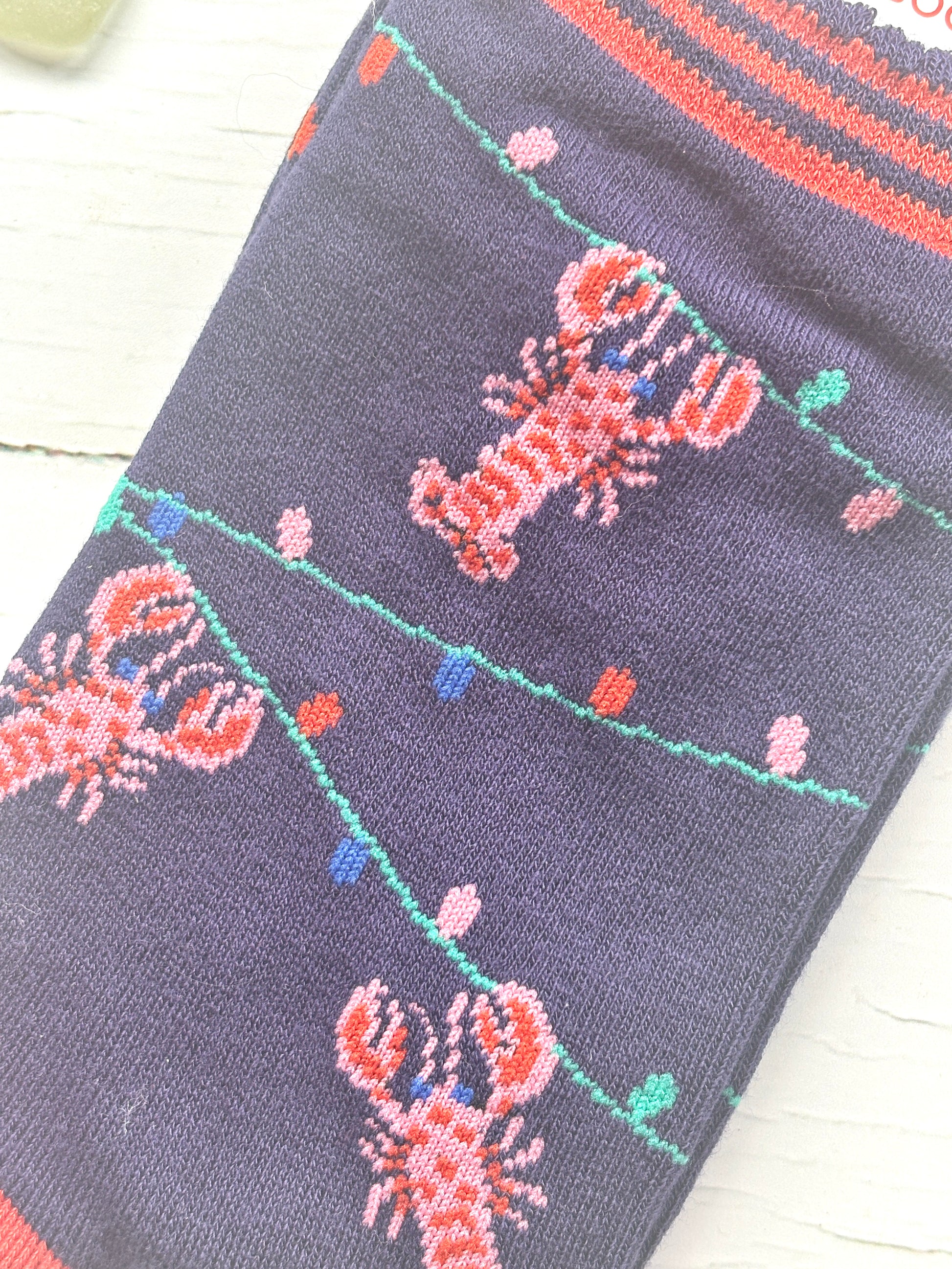 closeup shot of Christmas lobster socks woven pink lobsters on a navy blue background with colorful string lights coastal holiday apparel detail