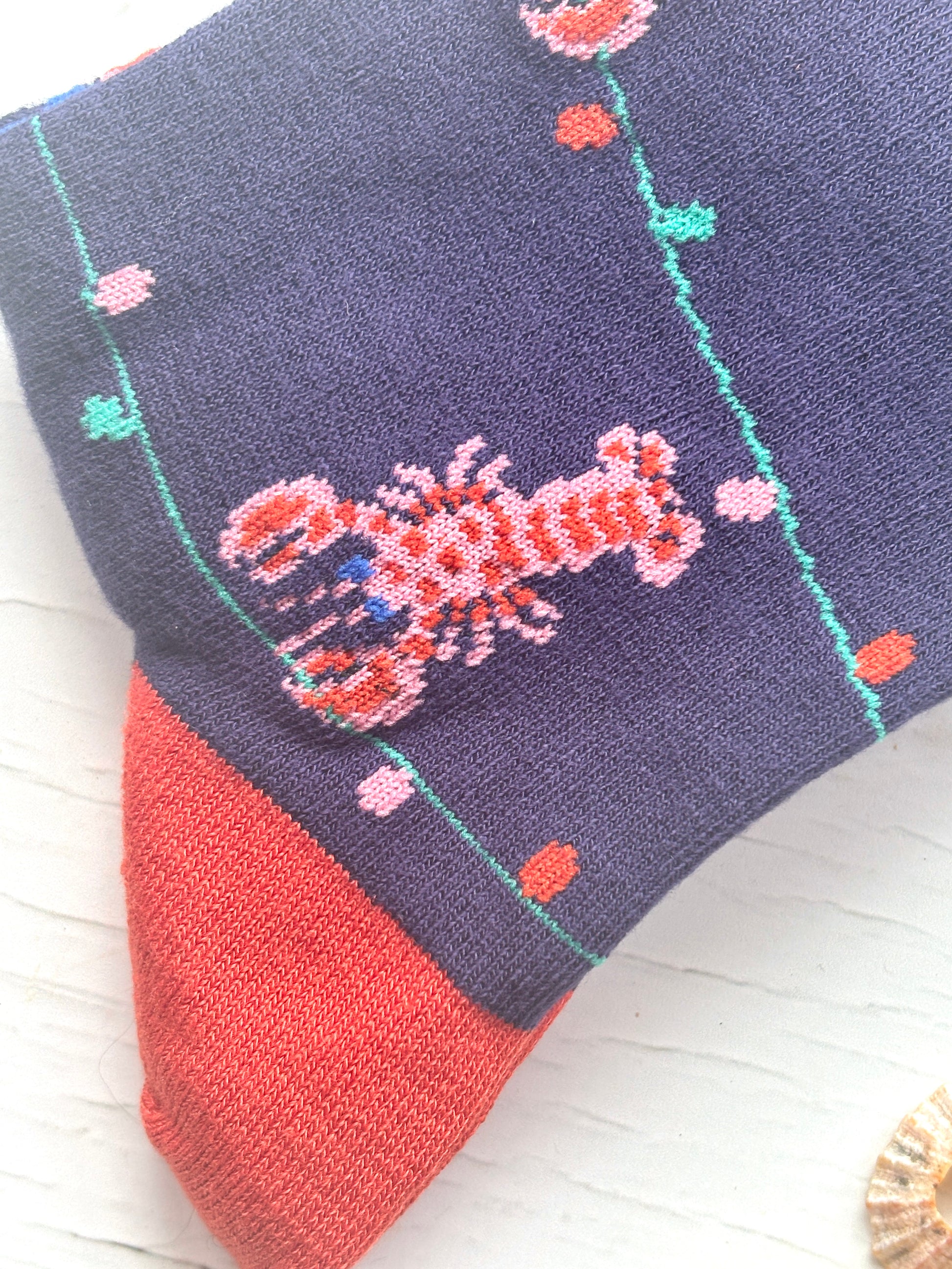 closeup shot of Christmas socks navy bamboo knit with a woven pink lobster and string of colorful lights red toe and heel