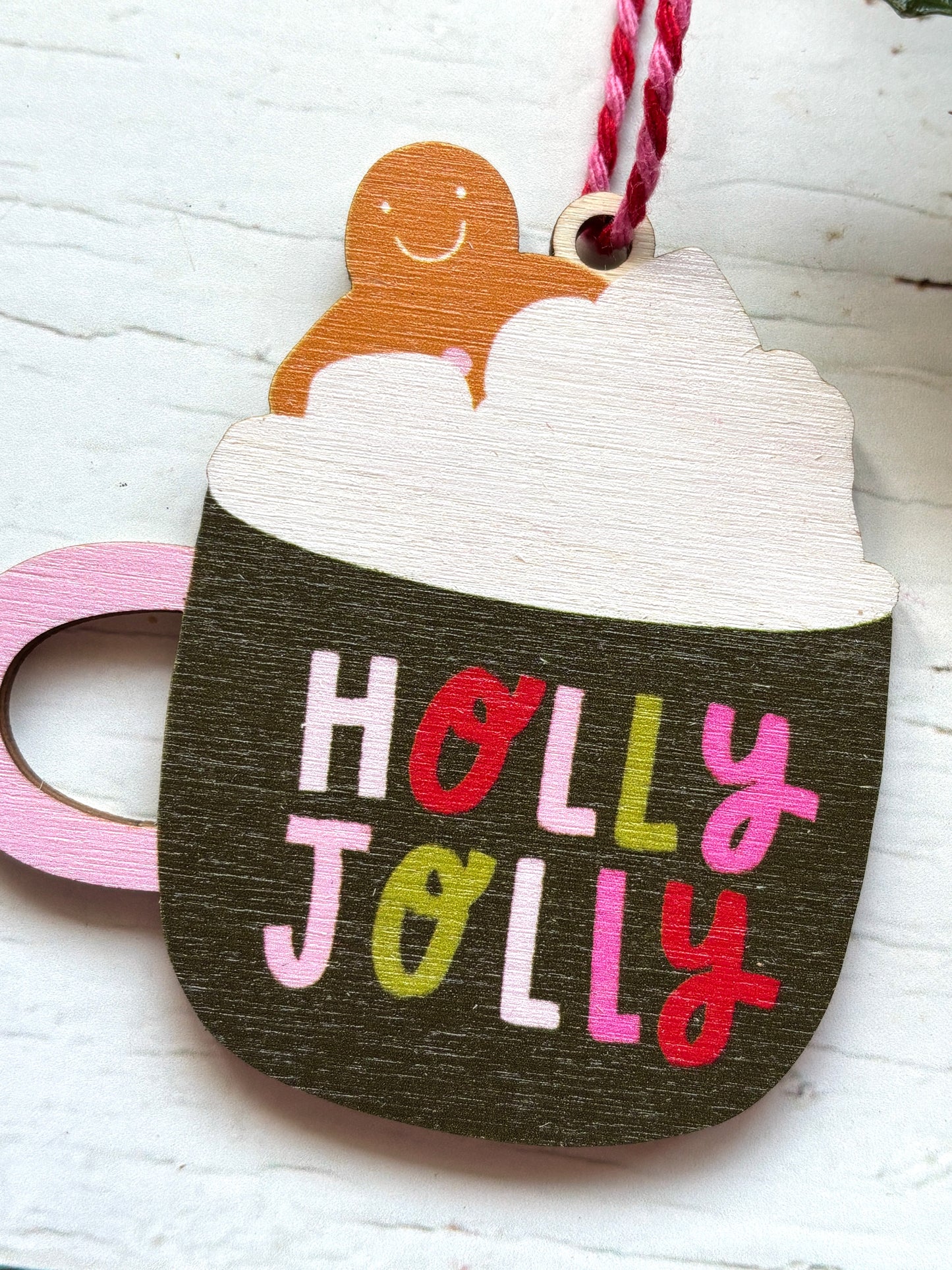 closeup shot of wooden 'Holly Jolly' hot chocolate mug ornament gingerbread man and whipped cream design festive drink Christmas tree decor