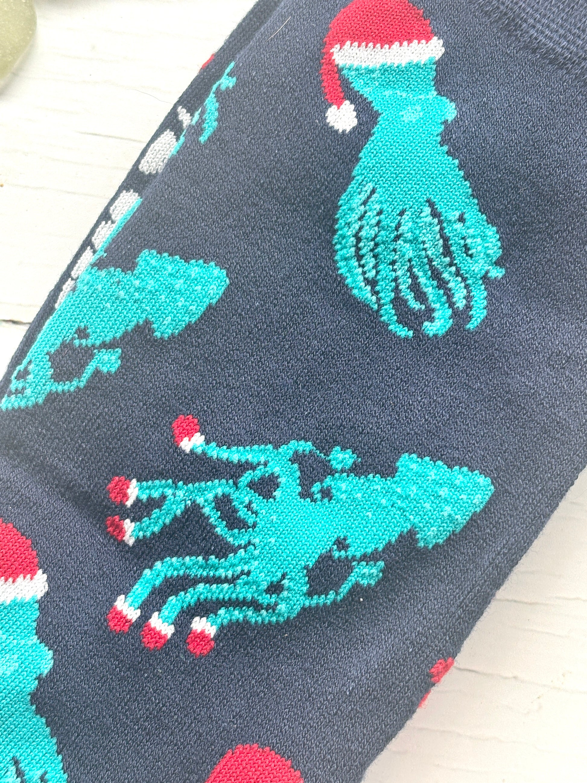 closeup shot of Christmas bamboo socks navy knit fabric with embroidered teal octopus/squid wearing a red Santa hat seaside holiday novelty