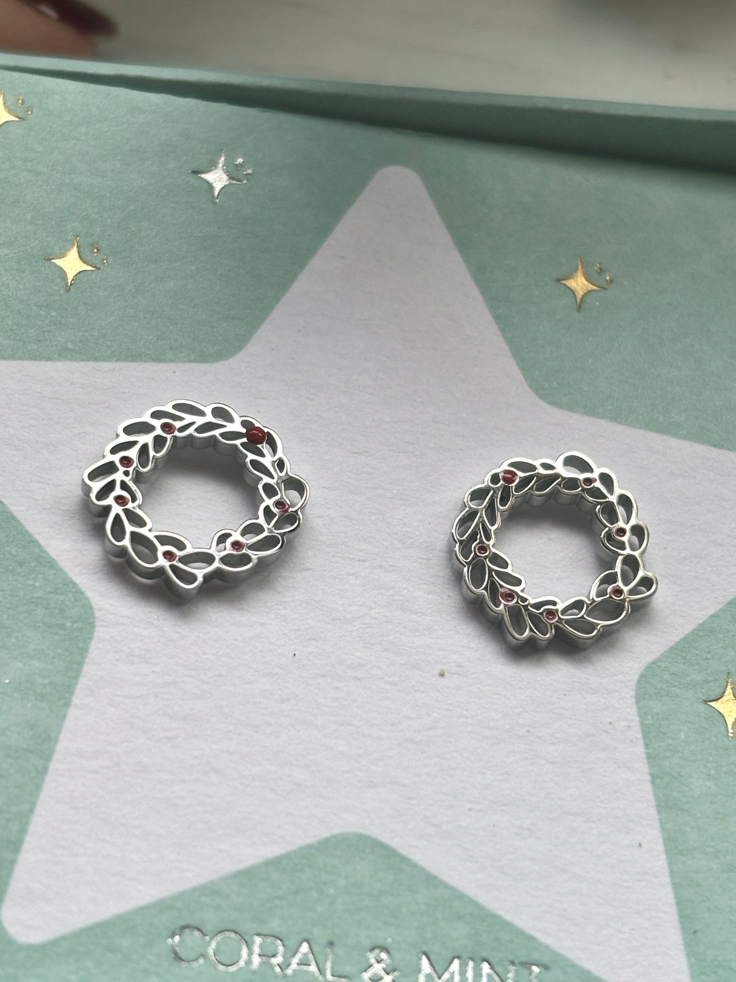Christmas wreath stud earrings—delicate silver leaves with red accents on festive card, perfect for holiday jewelry and gifting
