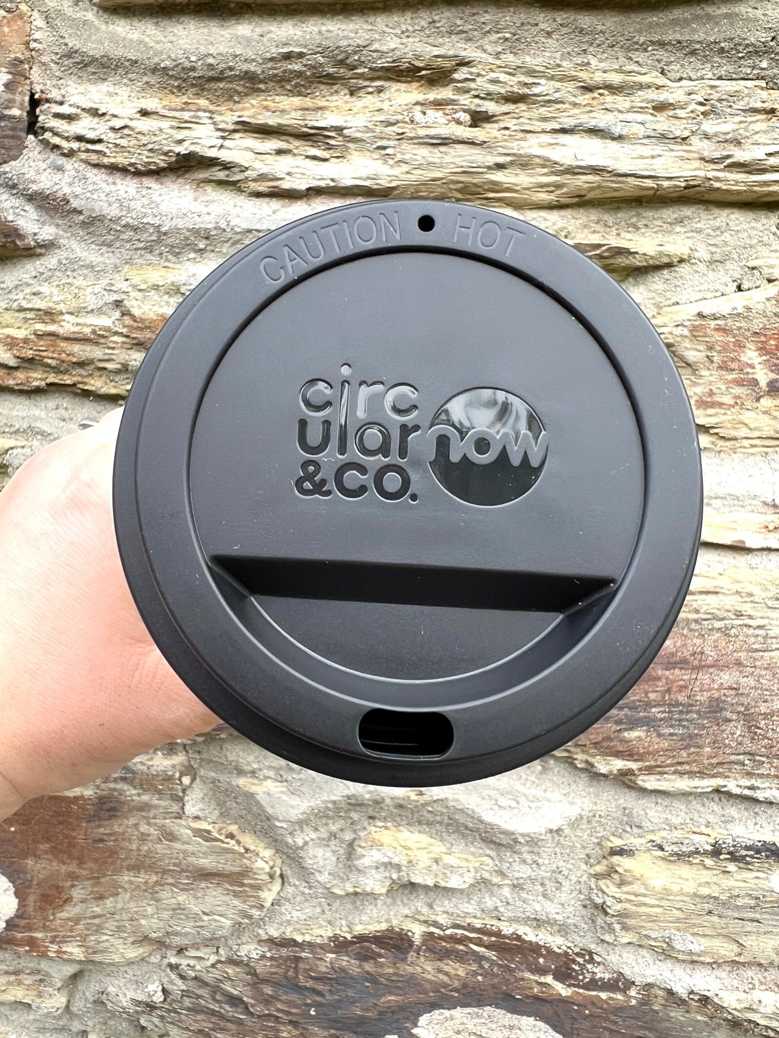 closeup shot of black lid for Circular&Co. Now Cup 12oz reusable coffee mug lid, 'CAUTION HOT' text, eco-friendly, recycled cup top