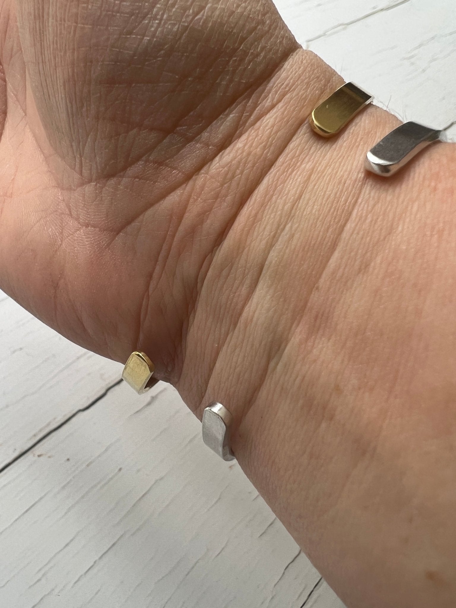 layered coordinate bracelets worn, brass aluminum geometric cuffs, minimal personalized accessory stack, contemporary jewelry