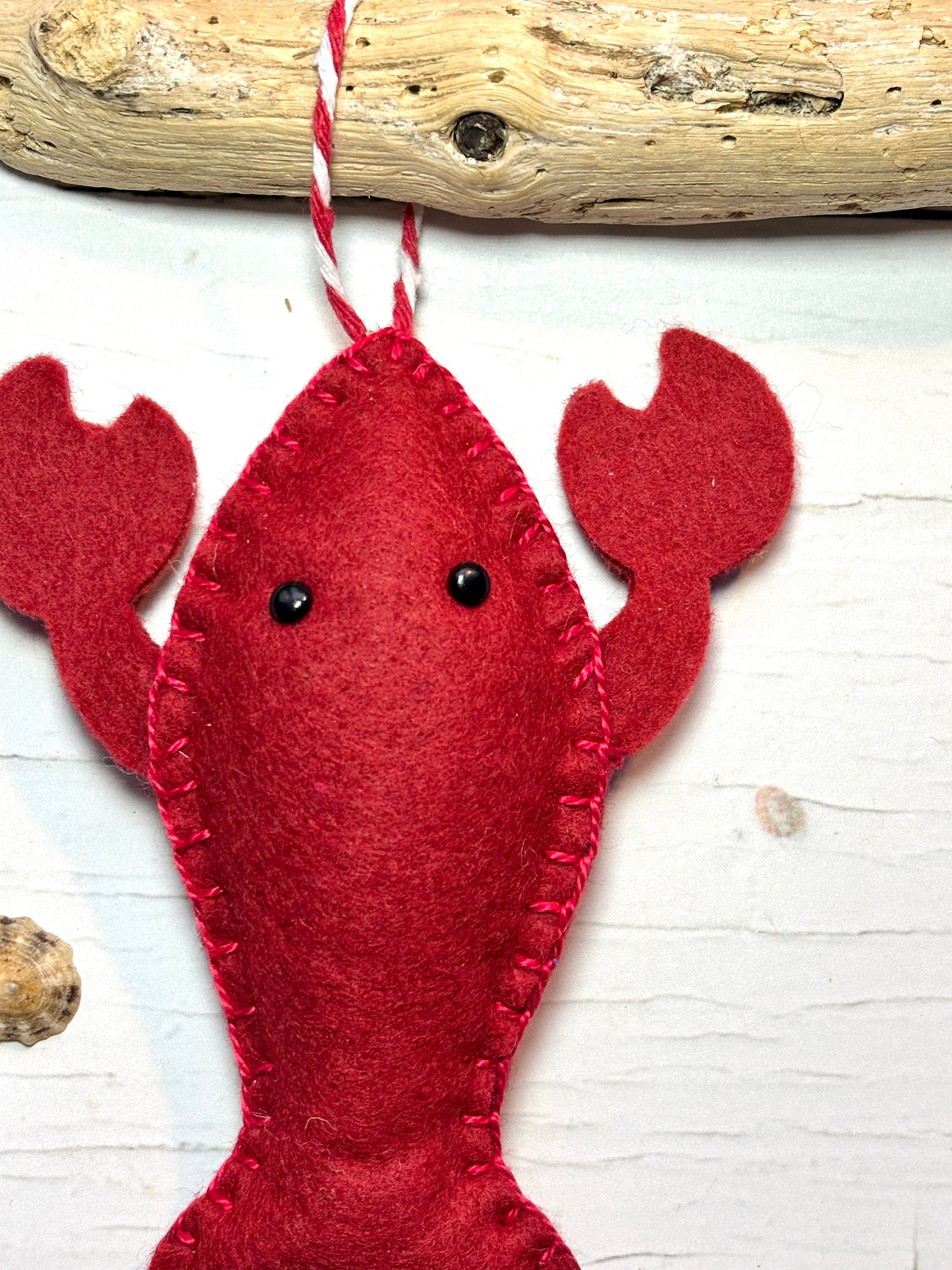 closeup shot of red felt lobster ornament head hand-stitched craft with black eyes, hanging from driftwood seaside Christmas decor