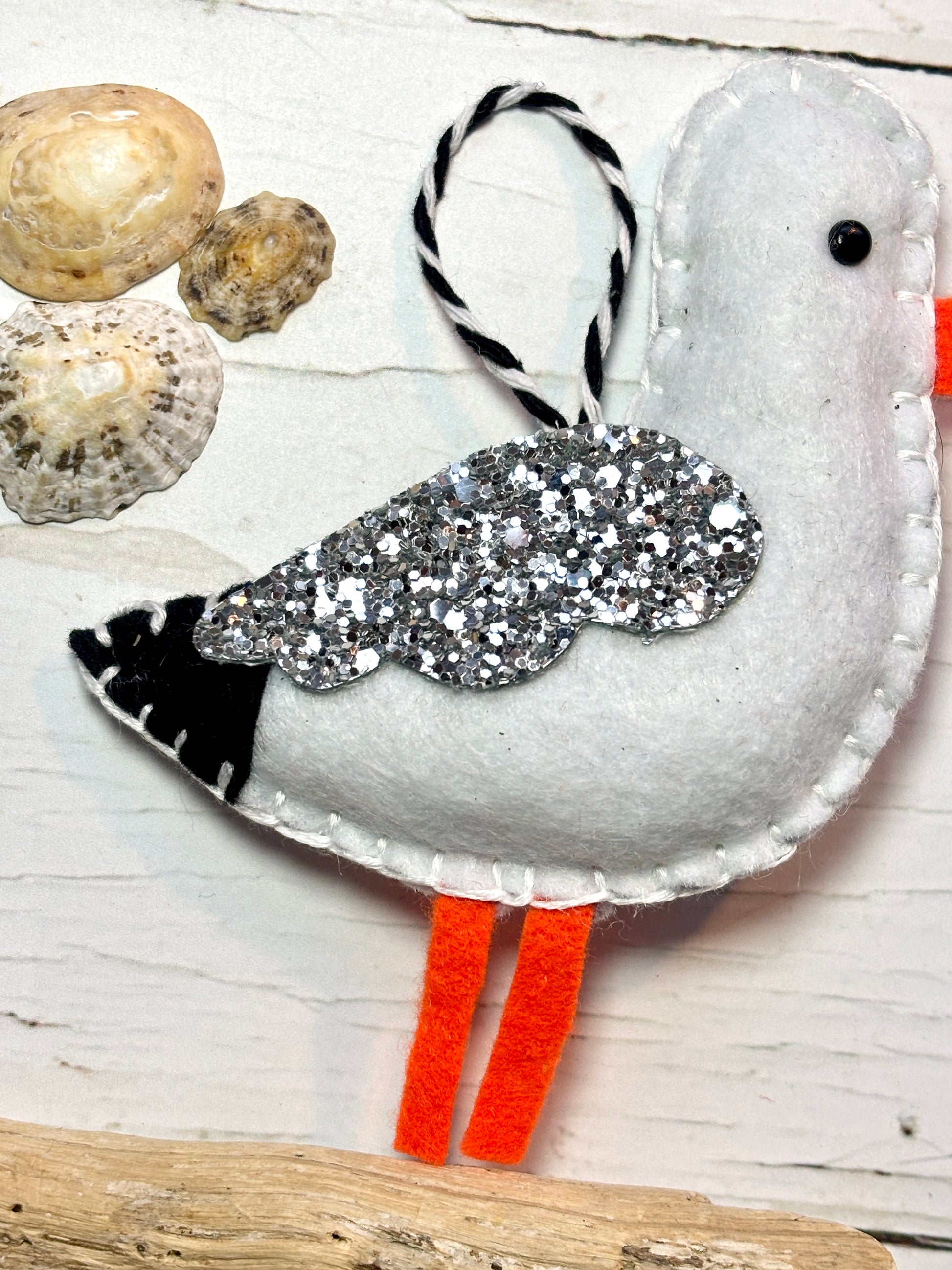 felt seagull ornament on driftwood with seashells, black, white, and orange coastal bird decor handstitched and glittered craft