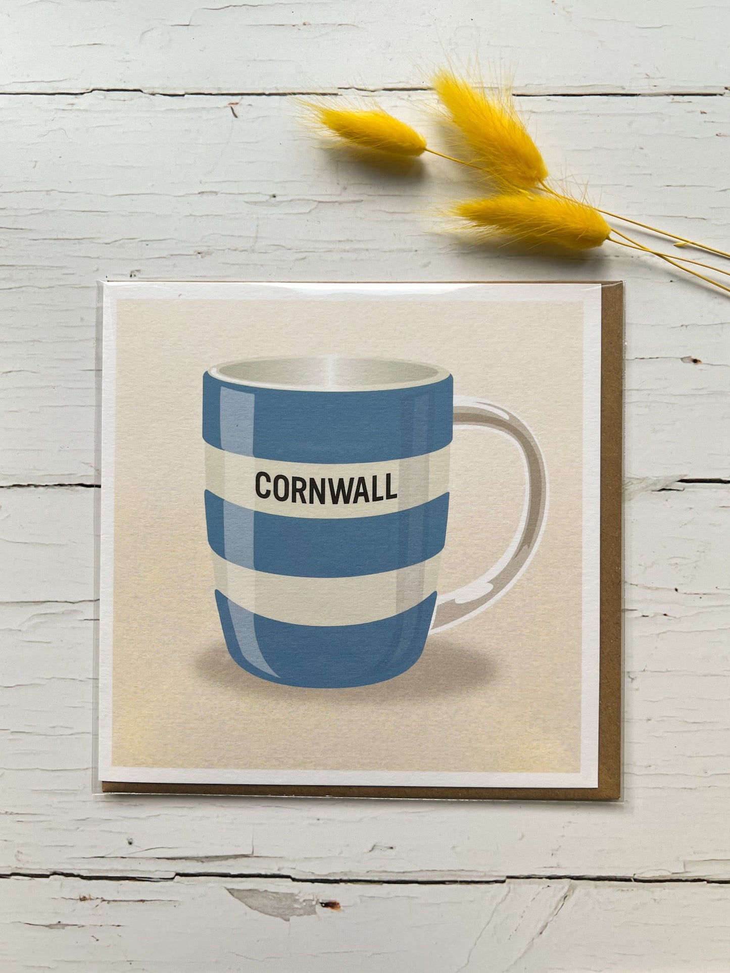 blue and white striped Cornwall coffee mug card, rustic wood background, kraft paper envelope, yellow floral stems