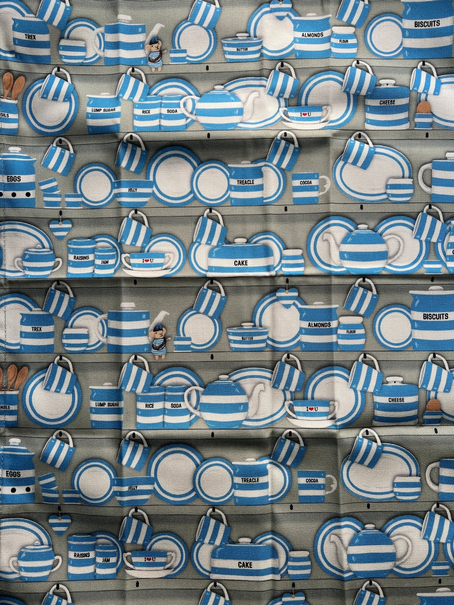 closeup shot of vintage-style Cornish kitchen textile with blue striped tableware pattern, labeled storage jars, retro fabric design