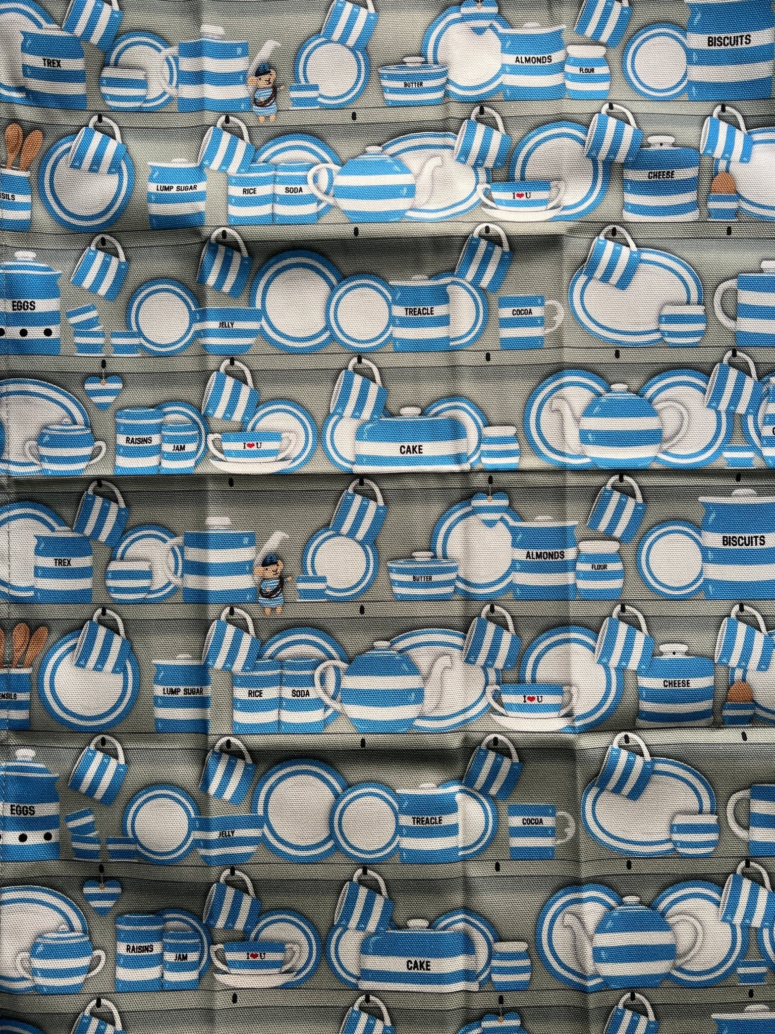 closeup shot of vintage-style Cornish kitchen textile with blue striped tableware pattern, labeled storage jars, retro fabric design