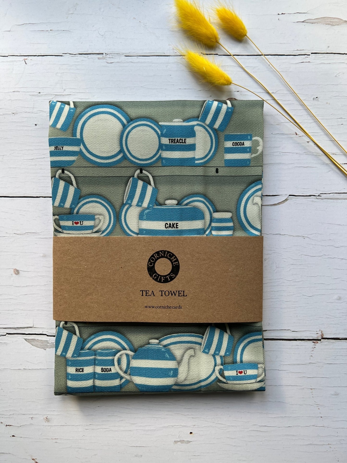 corniche gifts sage green tea towel with blue striped Cornish wrestler pattern, kraft band, dried flowers accent