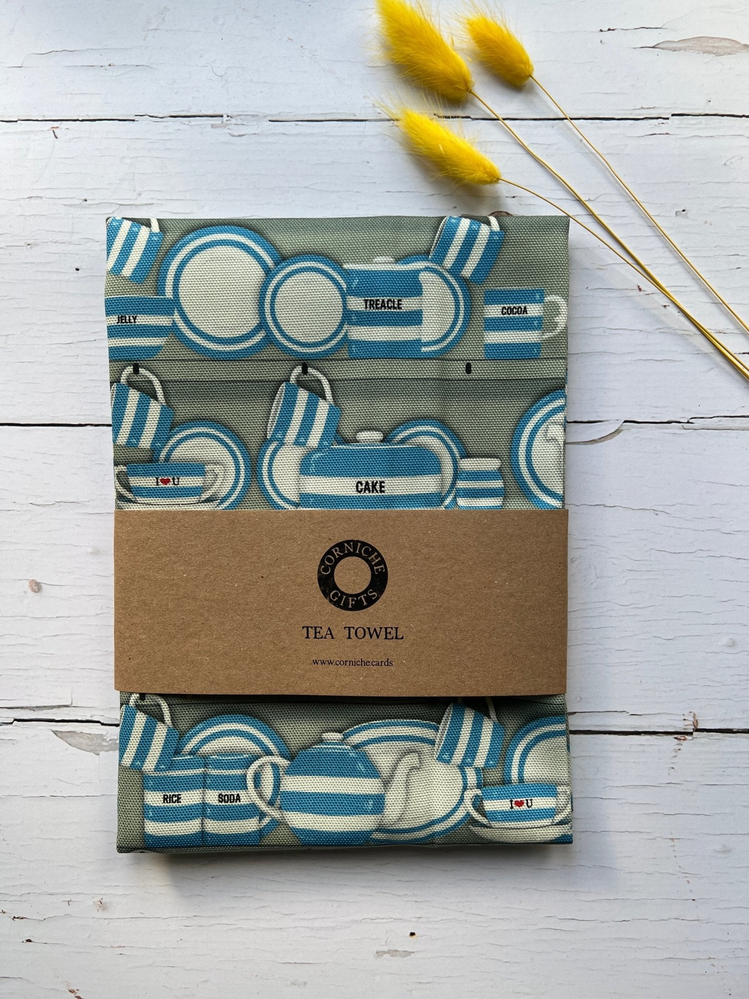 corniche gifts sage green tea towel with blue striped Cornish wrestler pattern, kraft band, dried flowers accent