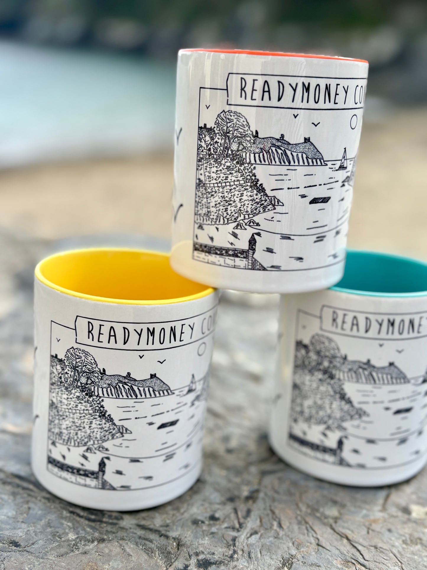 closeup shot of readymoney cove mugs with coastal line art, bold colors, and beachside vibe—perfect seaside gift or travel memento