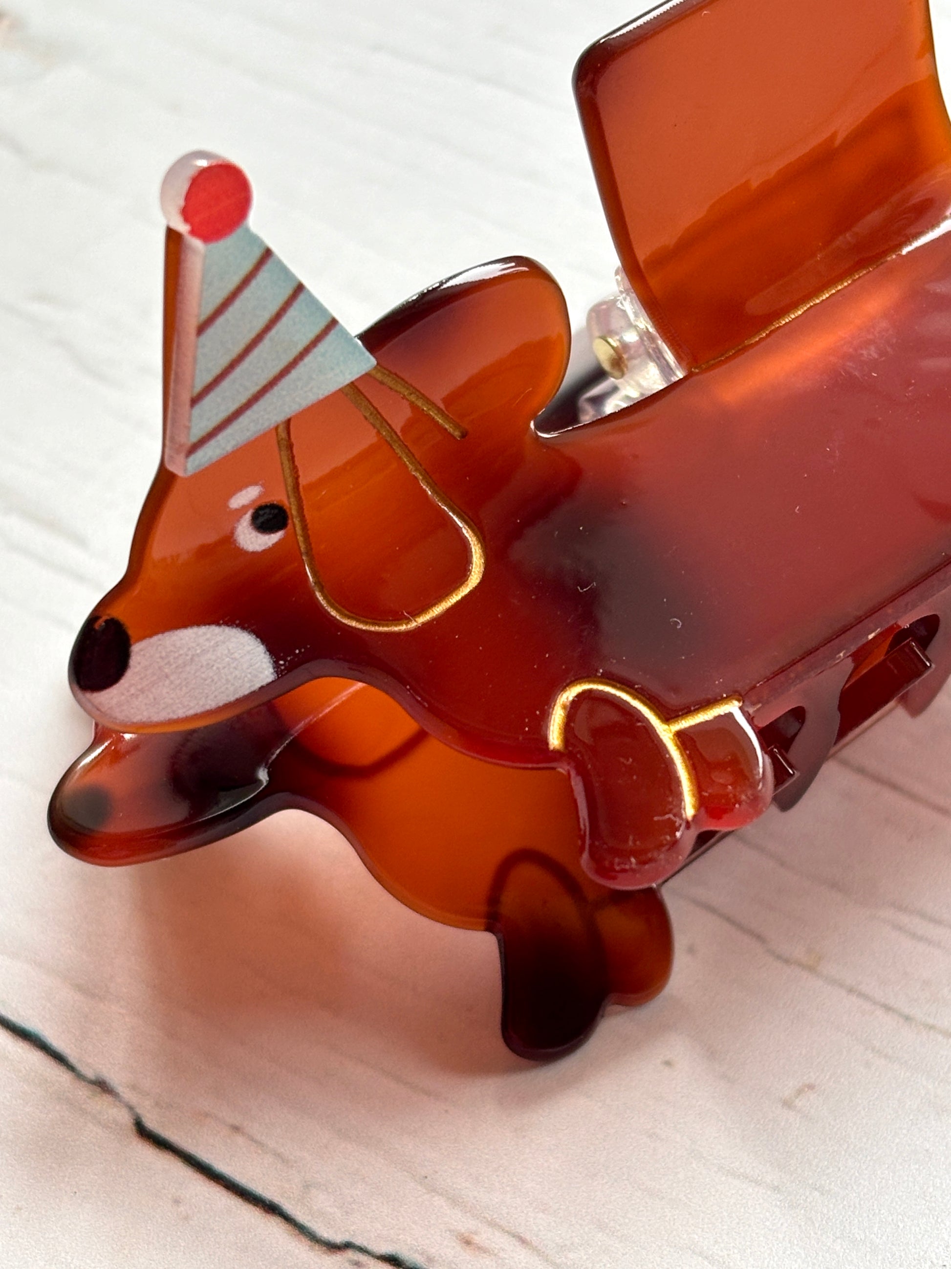 closeup shot of dachshund dog hair claw—translucent brown clip with party hat, gold trim, and secure grip for playful styling