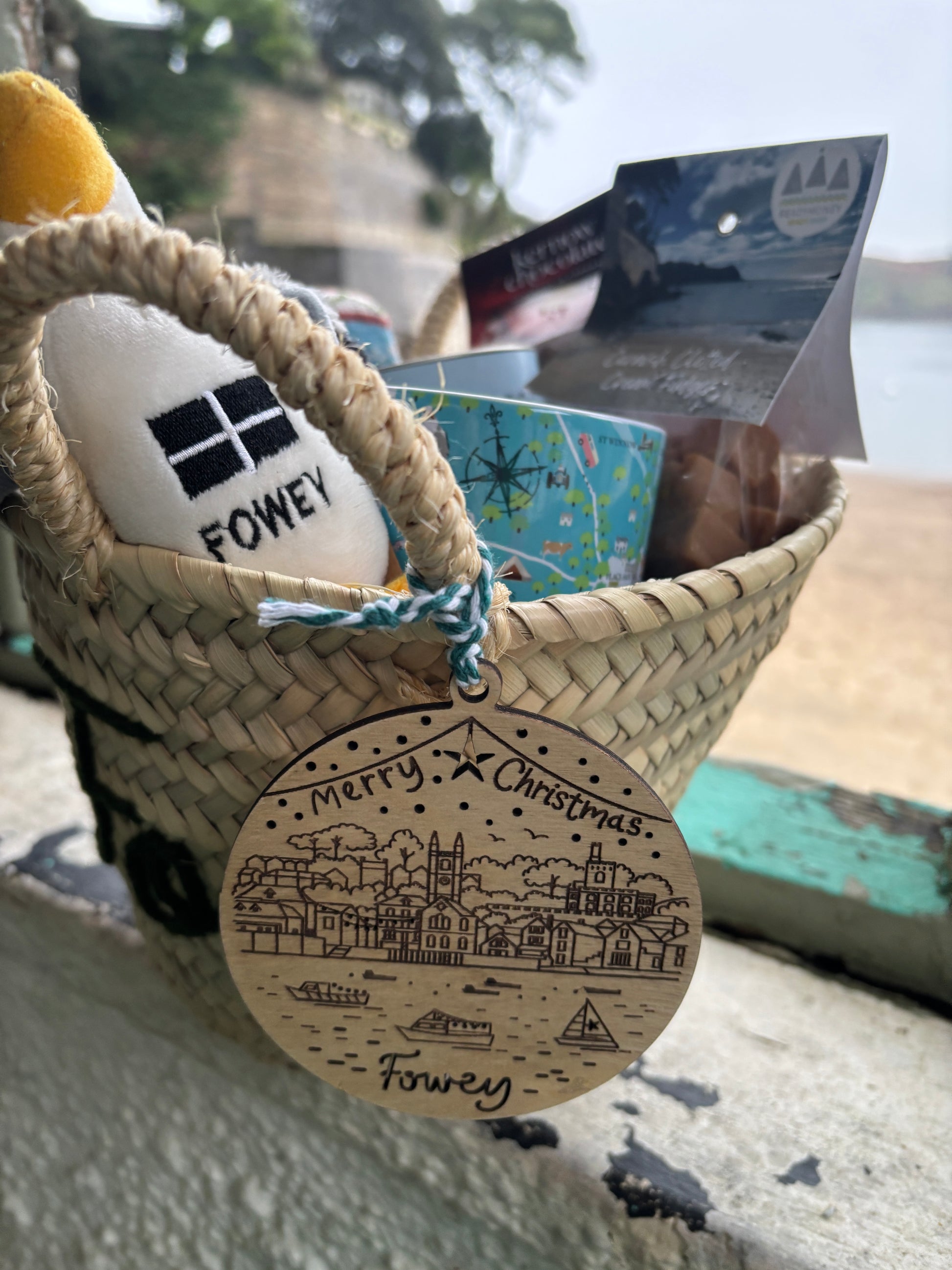 closeup shot of Fowey Christmas gift basket wooden Fowey ornament, penguin toy, and Kernow chocolate coastal holiday gift hamper
