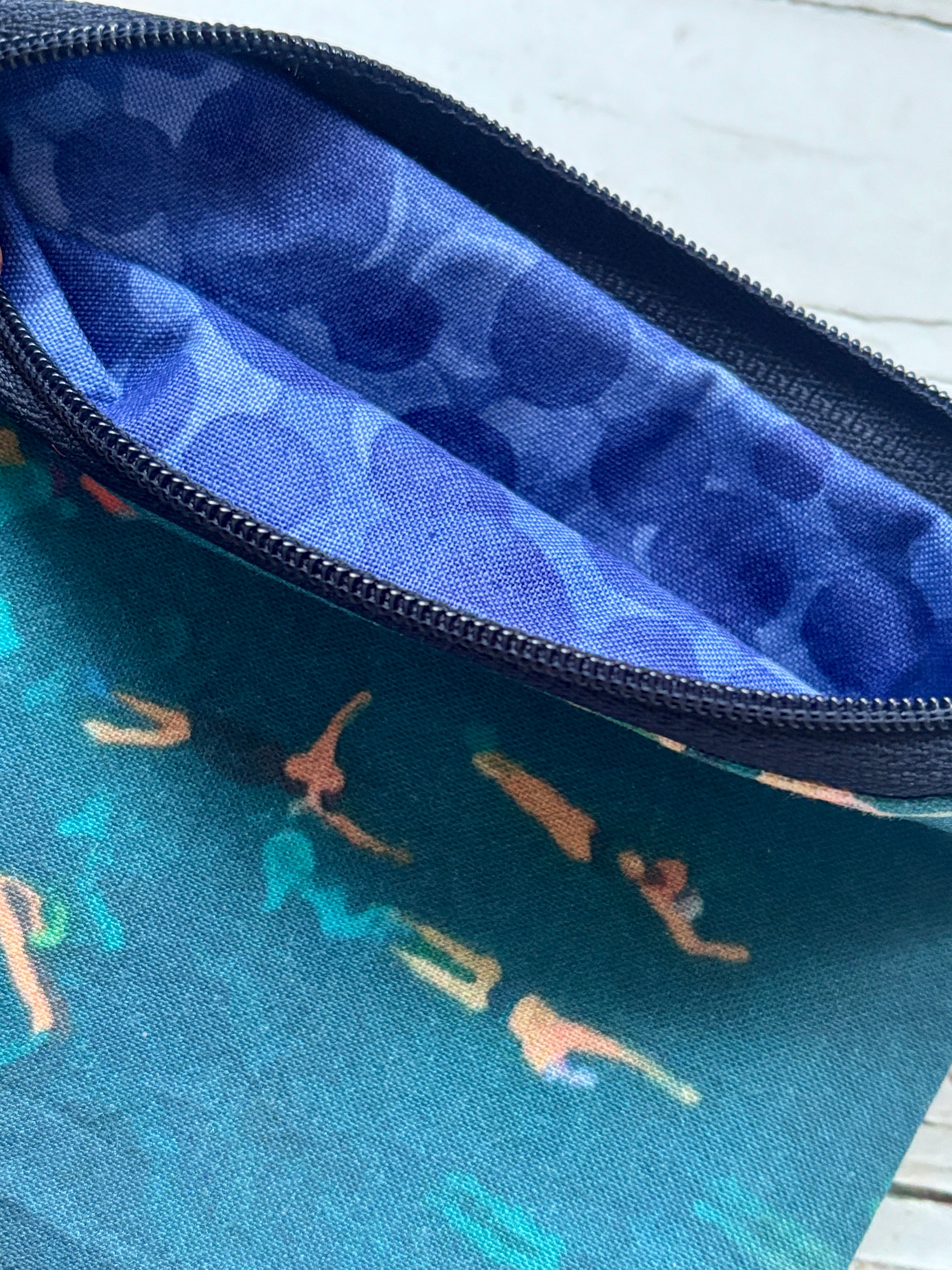 a zipped fabric purse with teal swimmers patterned fabric on the outside and blue bubbles patterned on the inside