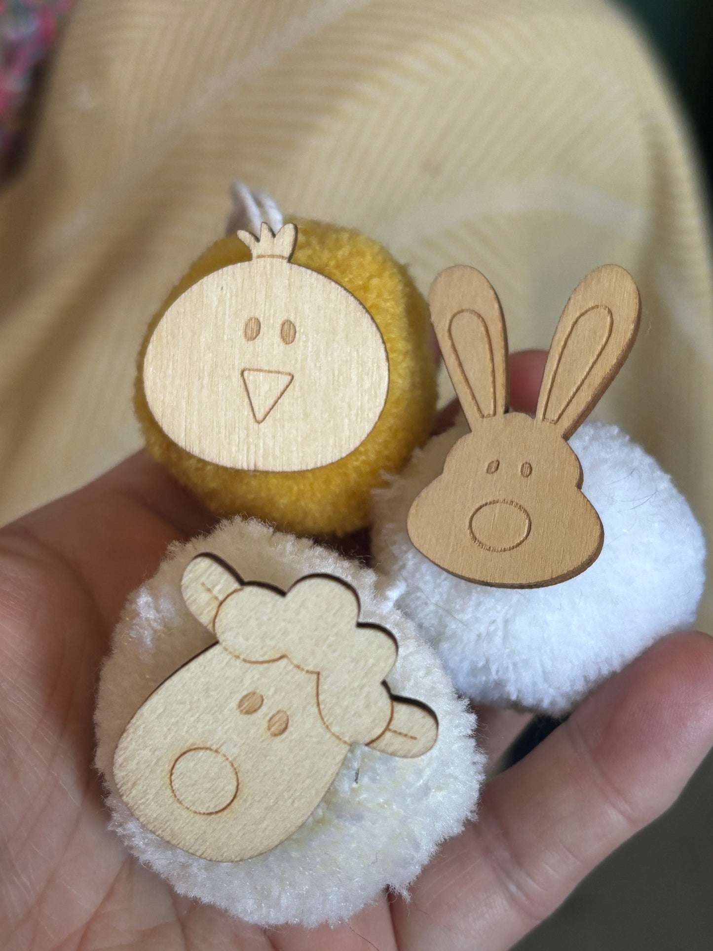 closeup shot of easter pom pom decorations held in hand - wooden bunny chick lamb on white yellow fluffy hanging ornaments
