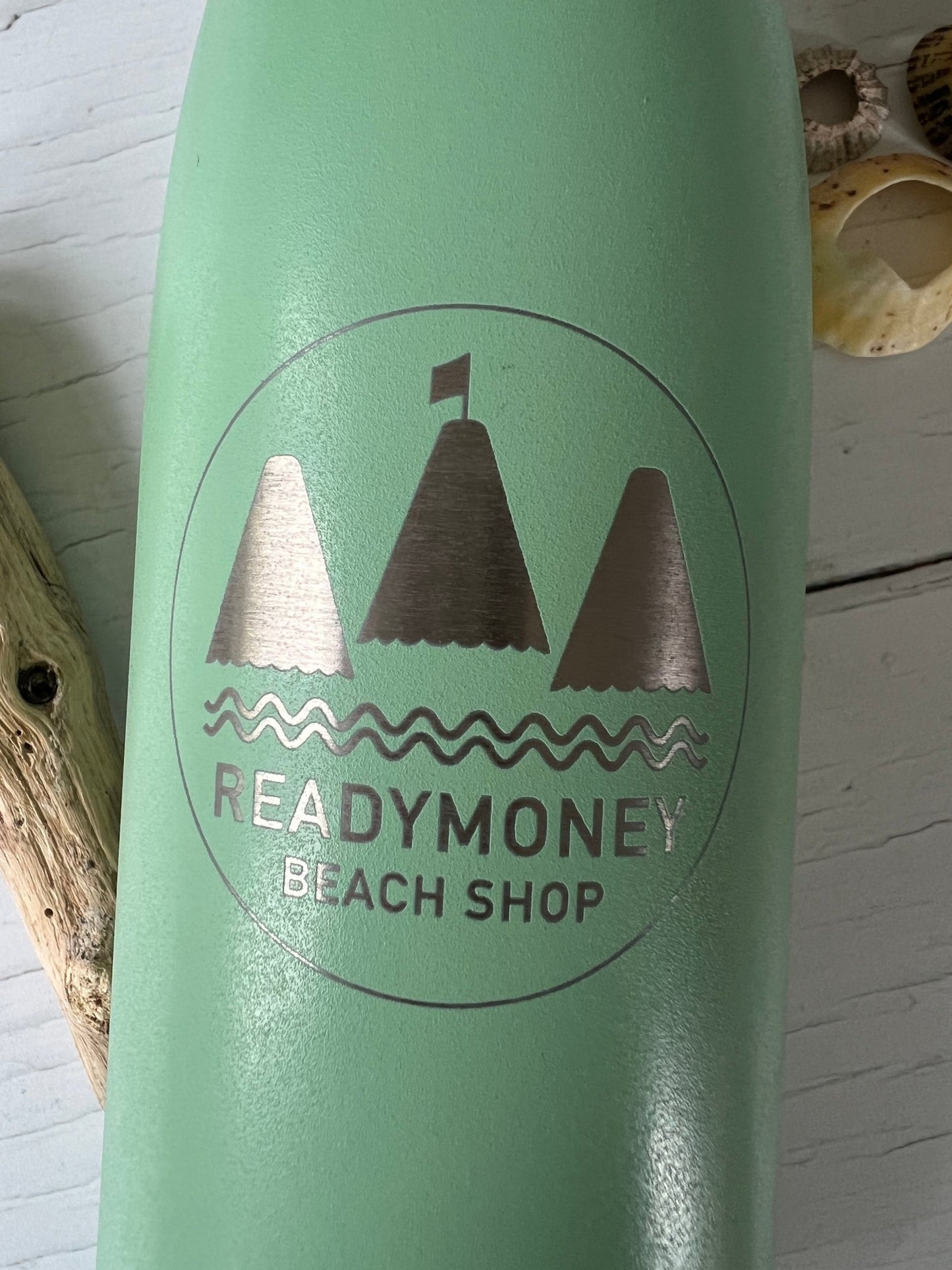 closeup shot of of engraved Readymoney beach shop logo on mint green insulated bottle with nautical sailboat design