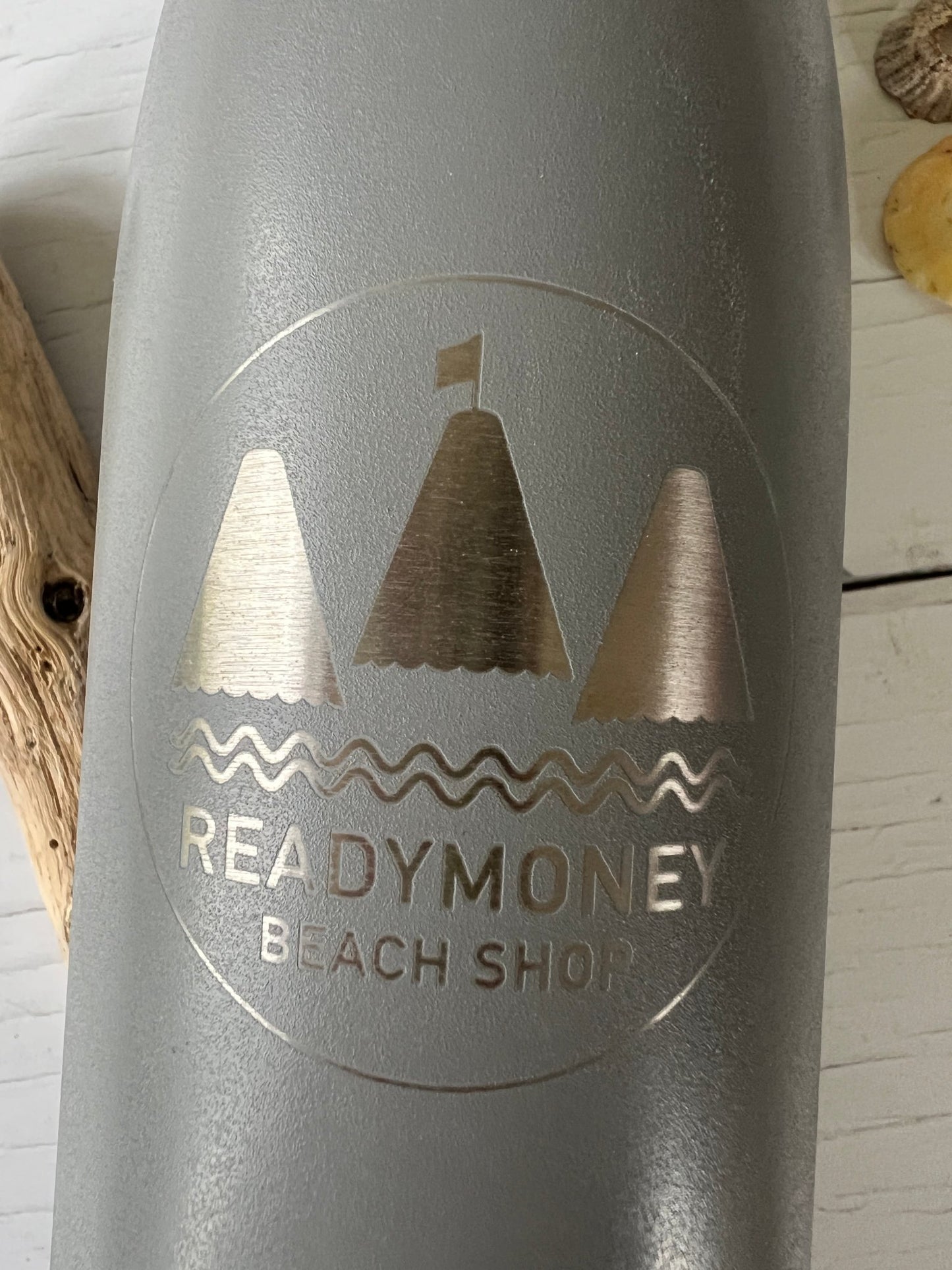 closeup shot of silver-grey insulated bottle with etched Readymoney beach shop logo featuring sailboats and waves