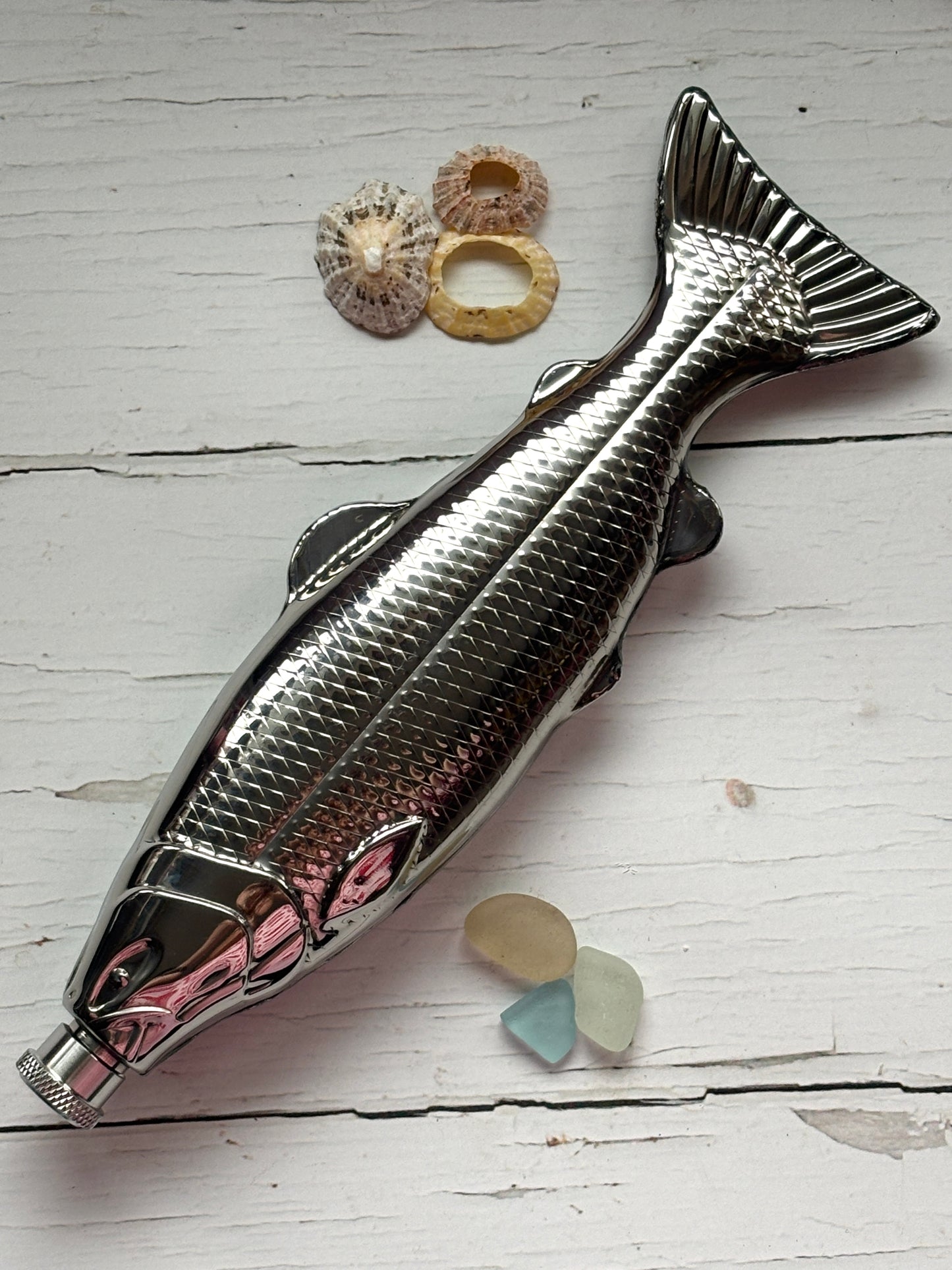stainless steel fish-shaped flask bottle with scale texture detail, nautical hip flask with sea glass and shells