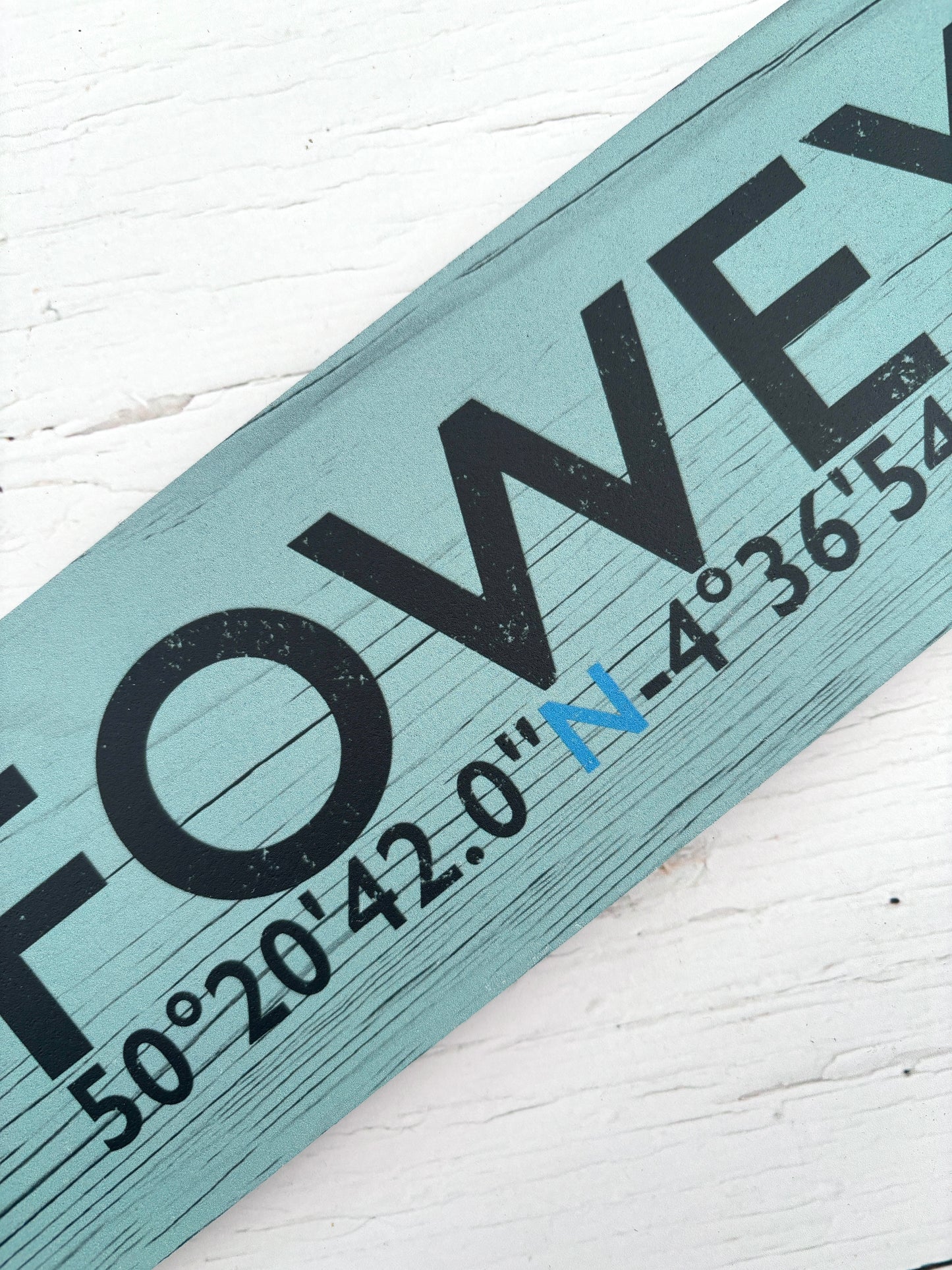 closeup shot of Fowey sign detail of coordinates and Fowey text on calm green distressed wooden arrow Coastal souvenir