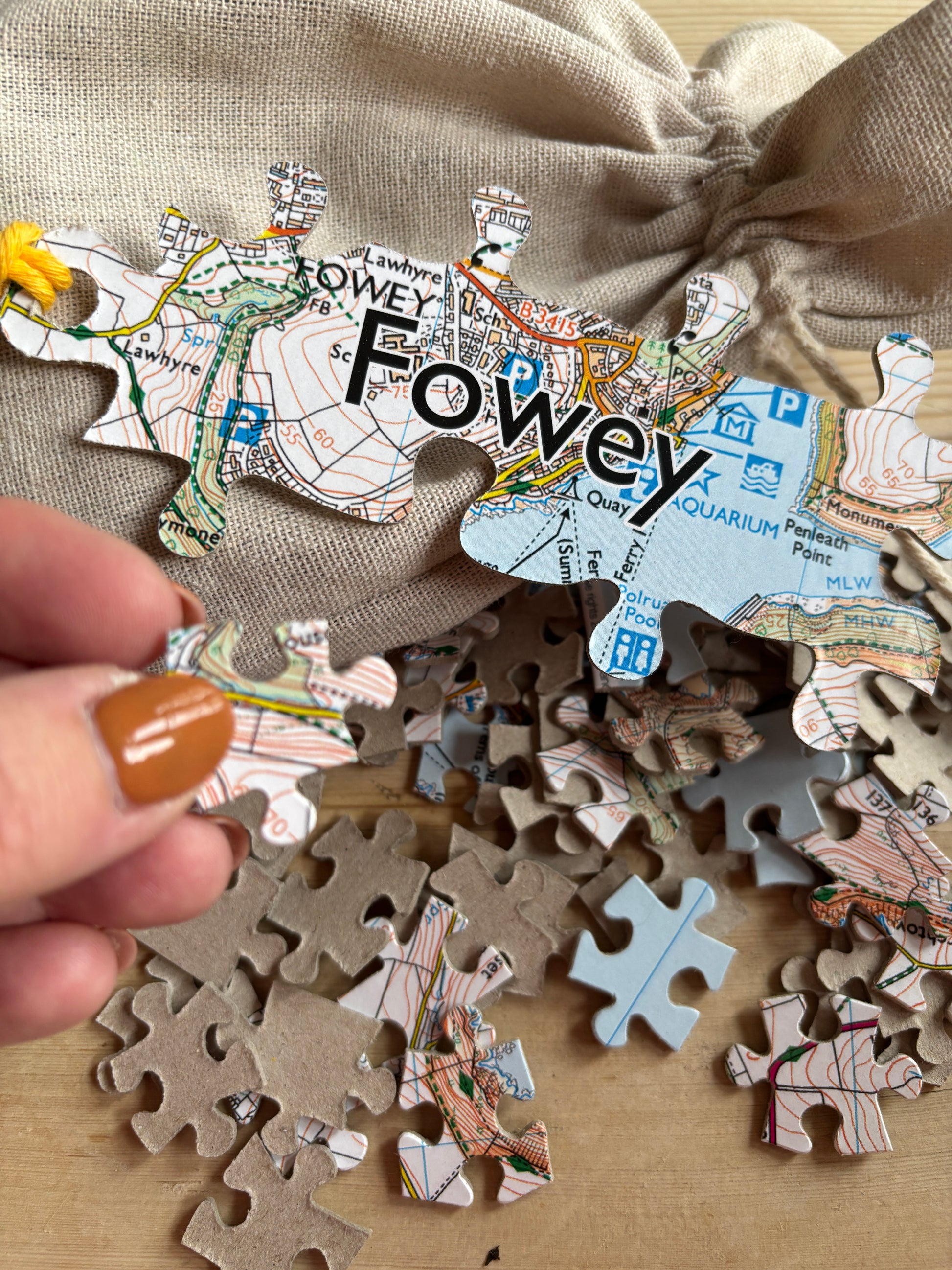 closeup shot of Fowey map puzzle hand holding a map-printed, lizard-shaped jigsaw piece Cornwall souvenir game detail, with calico bag