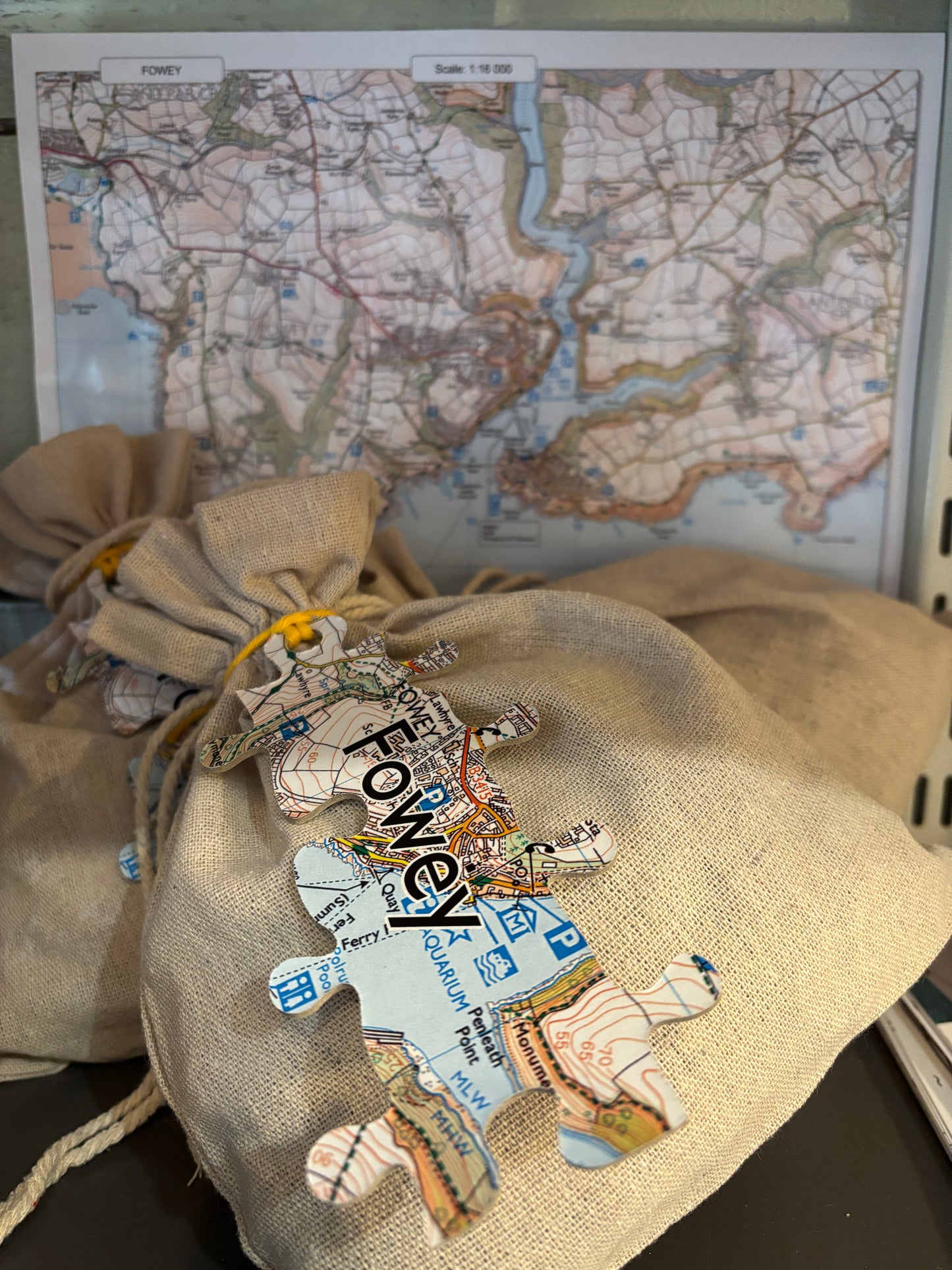 Fowey map puzzle stack multiple calico bags with lizard-shaped, map-printed jigsaw tags Cornwall souvenir game display with background map