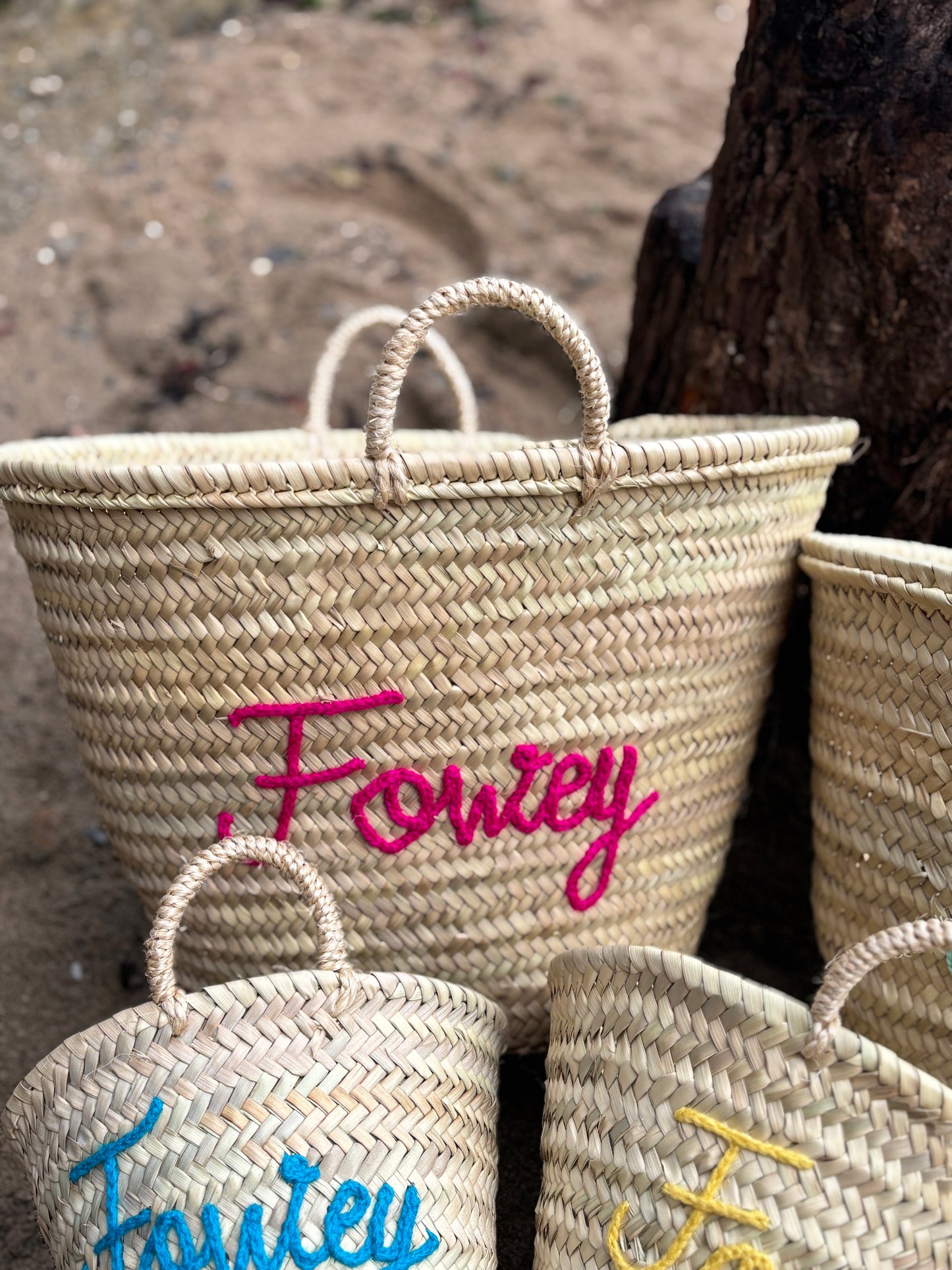 hand-woven straw maxi basket bag with Fowey fuchsia pink embroidery customizable chic beach tote on a sandy beach
