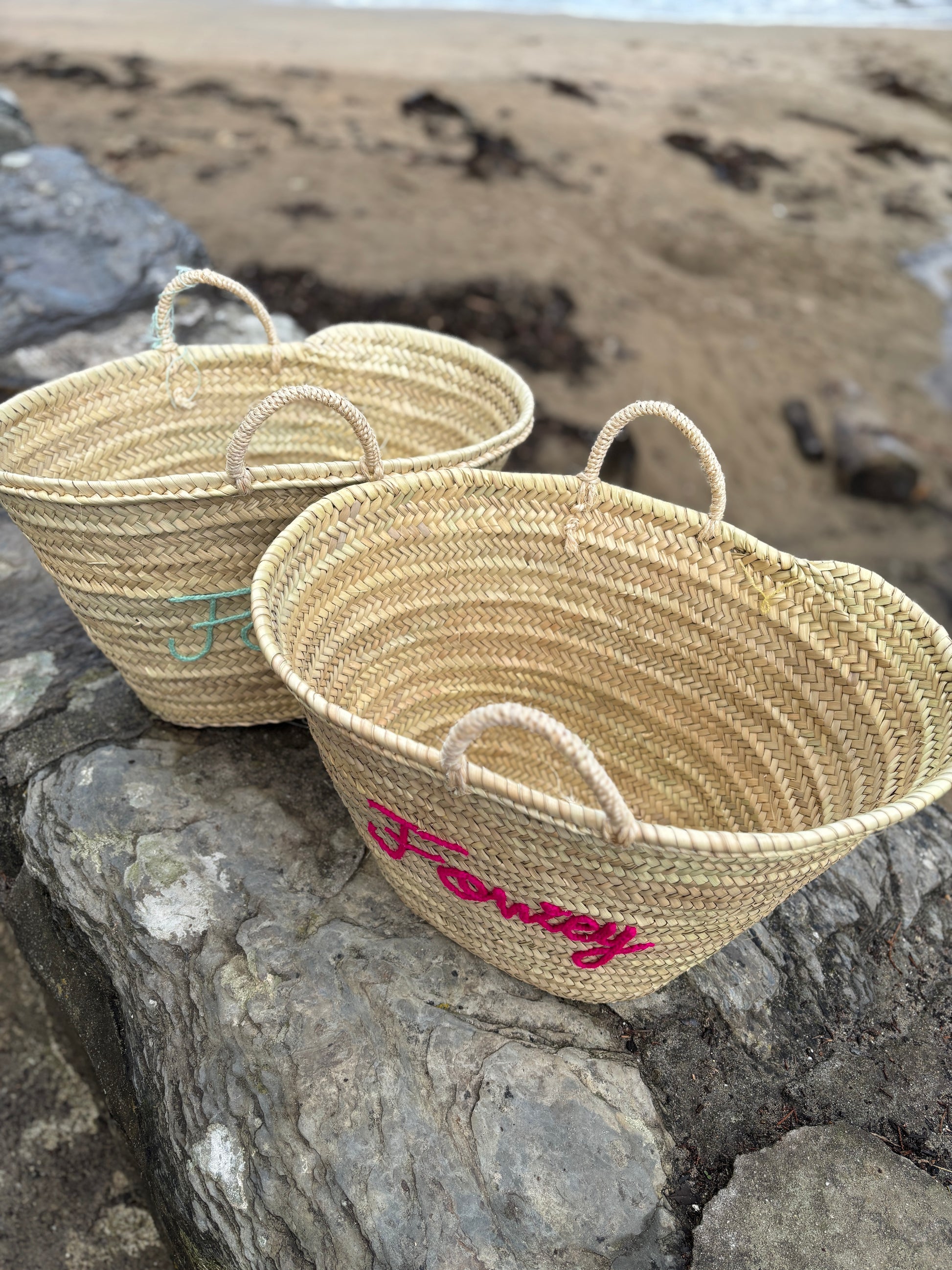 pair of customized straw beach totes with Fowey hand-embroidered in fuchsia and seafoam green coastal holiday accessories