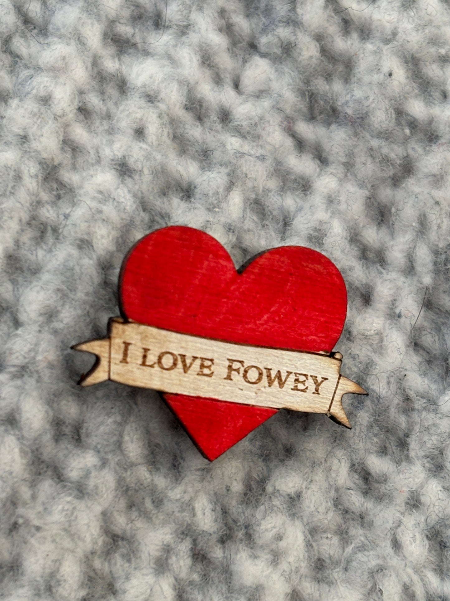 closeup shot of handmade red heart wooden pin badge with “I LOVE FOWEY” engraving—eco-friendly coastal keepsake gift
