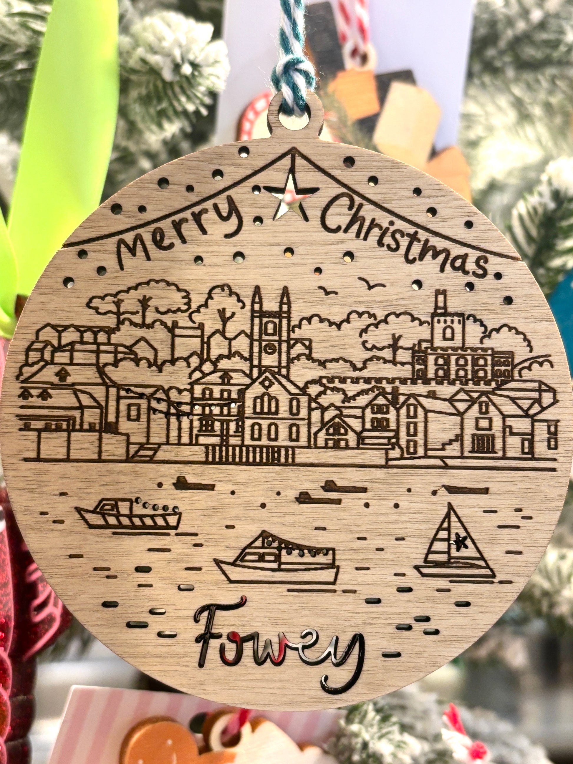 closeup shot of wooden Fowey bauble showing church tower, hillside homes, sailing boats, Cornish coastal Christmas ornament