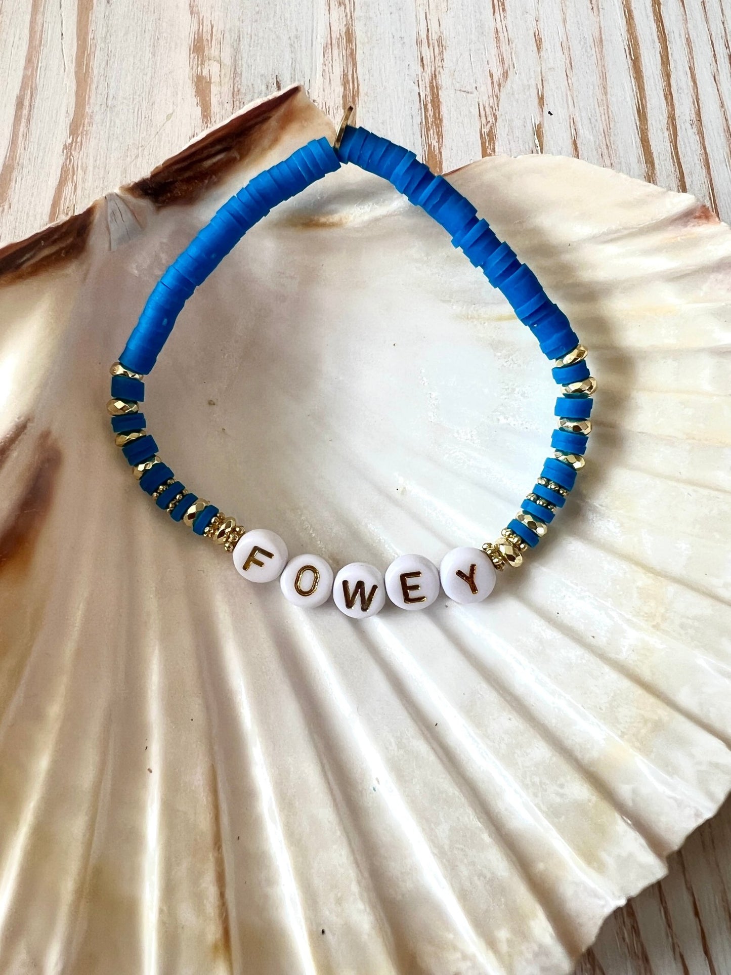 stylish sky blue beaded bracelet featuring FOWEY letter beads, gold accents, seashell background, coastal boho jewelry