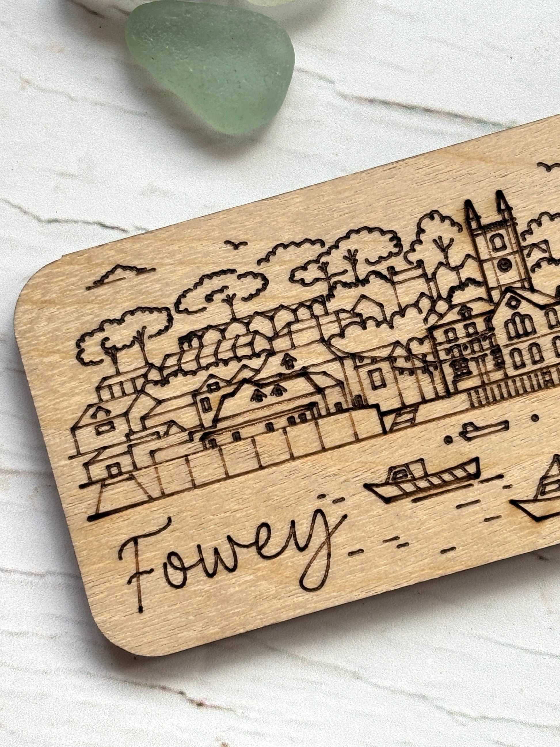 closeup shot of engraved Fowey magnet, detailed Cornwall town etching, wooden harbor scene, laser cut coastal illustration