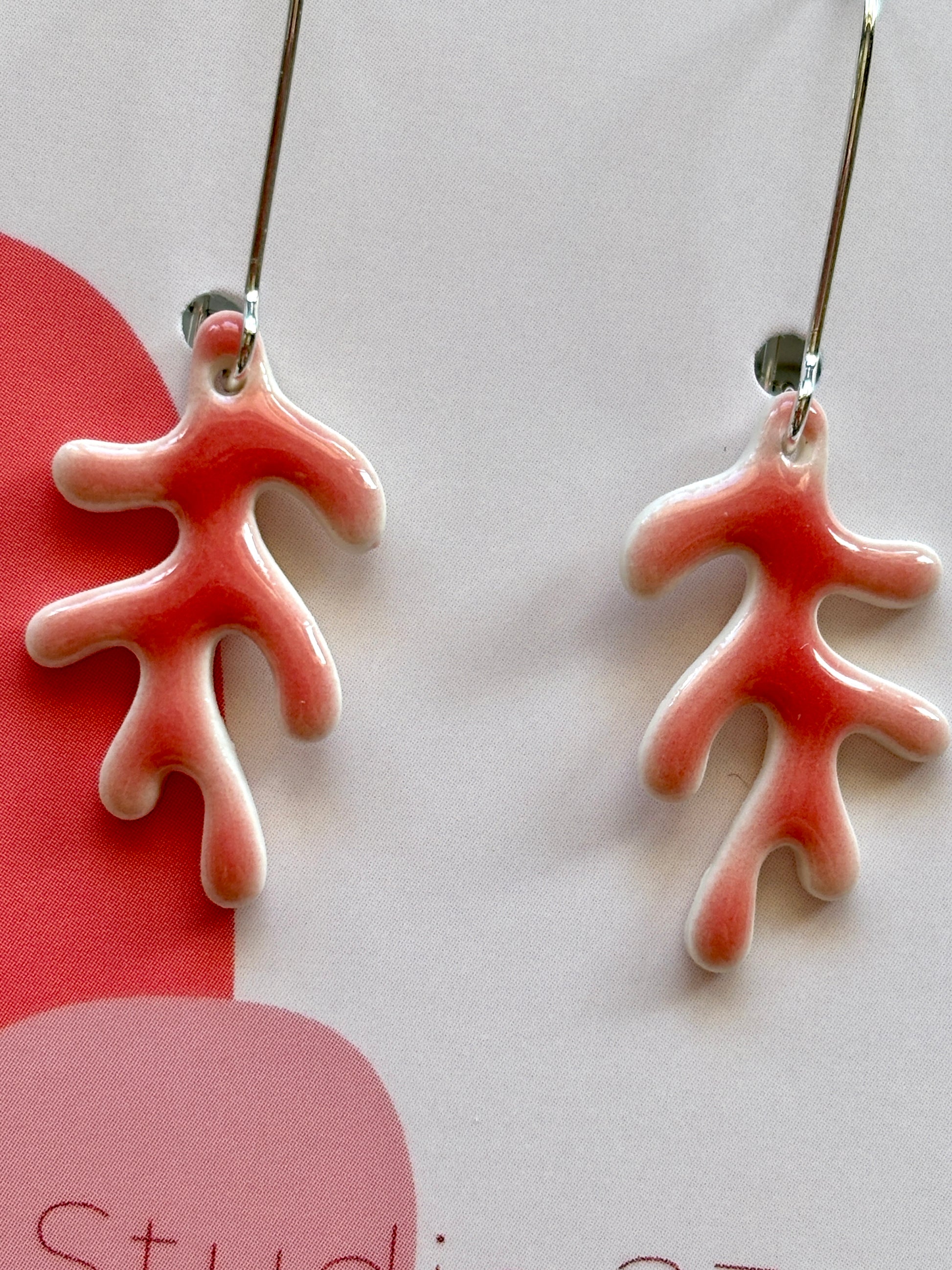 closeup shot of glazed porcelain drop earrings – coral-inspired ceramic dangles with red-white gradient, lightweight and artful