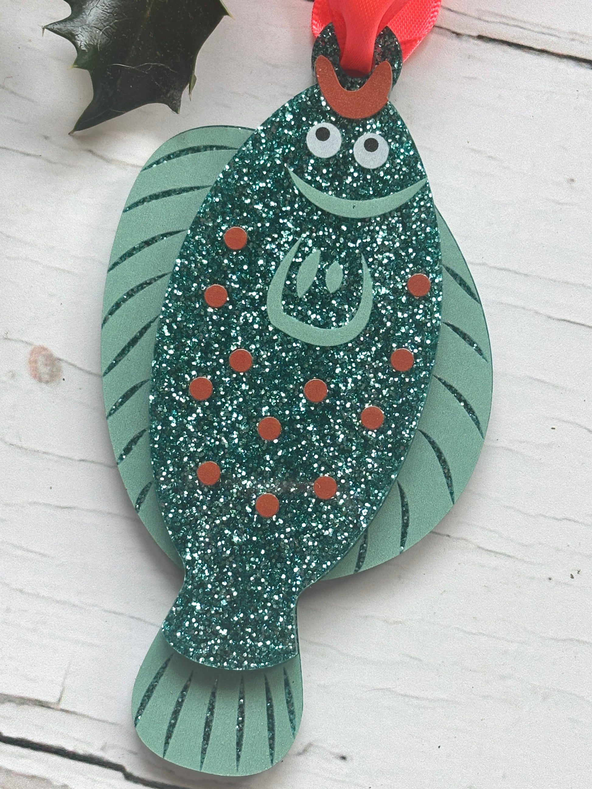 glittery teal plaice fish Christmas decoration with orange dots and red ribbon, fun coastal festive tree ornament