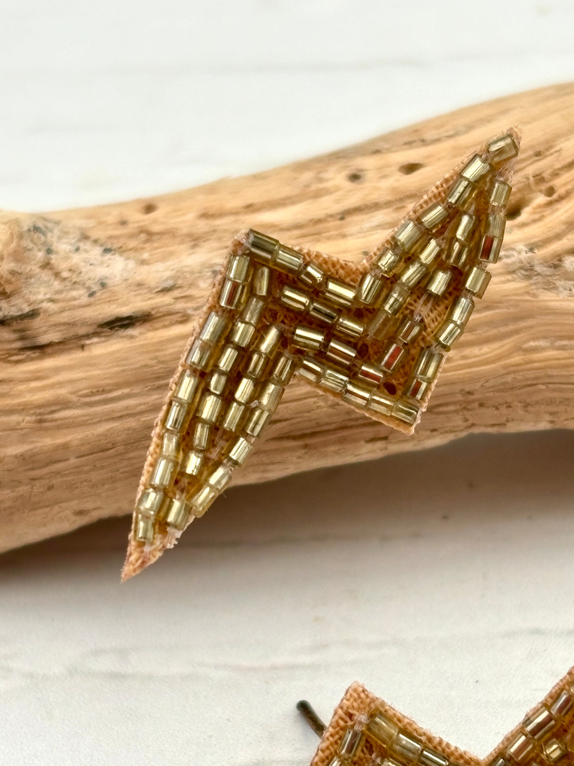closeup shot of a single gold beaded lightning bolt earring hand embroidered jewellery with seed beads for a statement and glam rock look