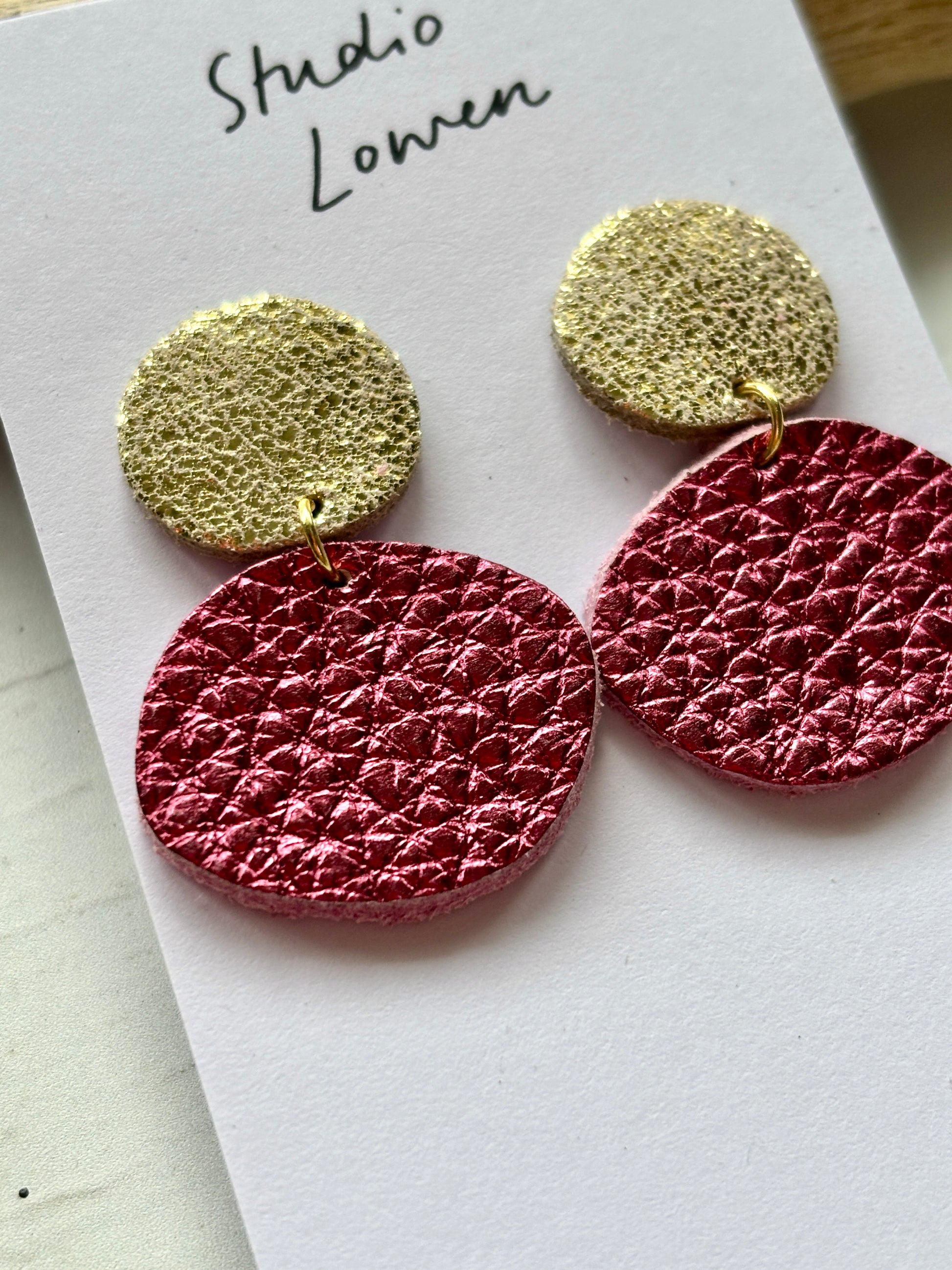 closeup shot of metallic rose pink leatherette dangle earrings gold textured stud modern fashion statement jewelry