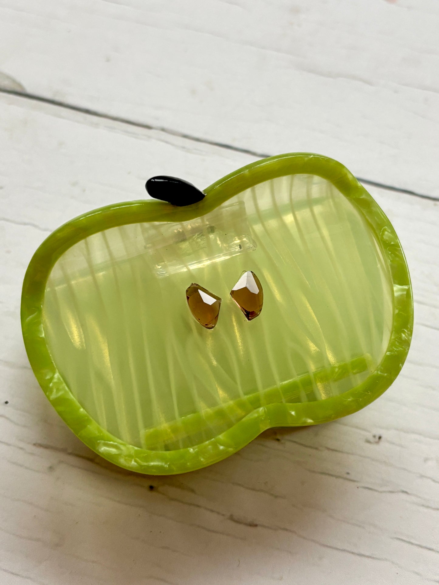 detail view of green apple hair claw—striped body, gem seeds, glossy finish for playful, secure styling