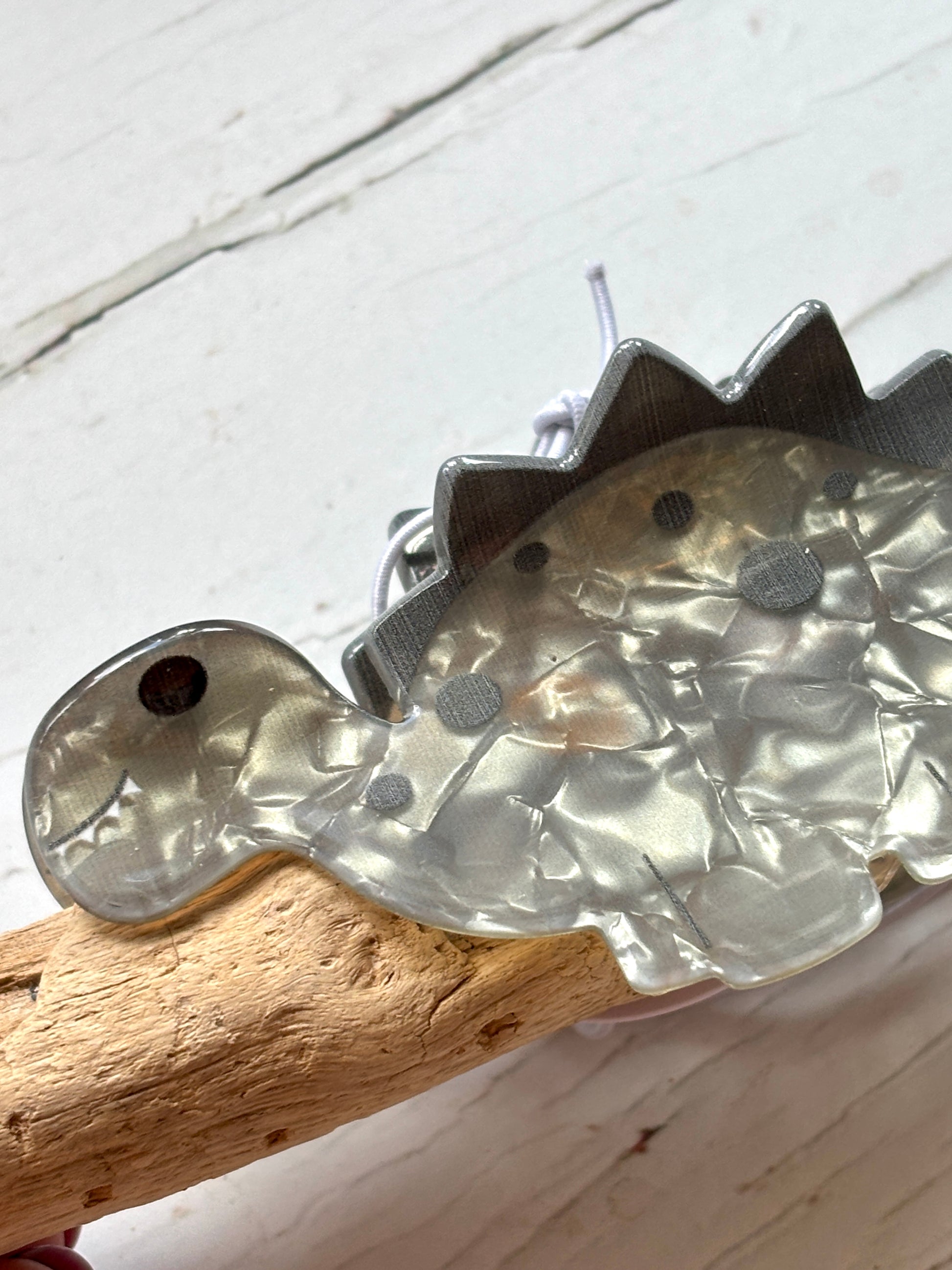 closeup shot on a marbled grey acrylic Stegosaurus hair claw clip unique novelty hair accessory or dino hair decor on driftwood