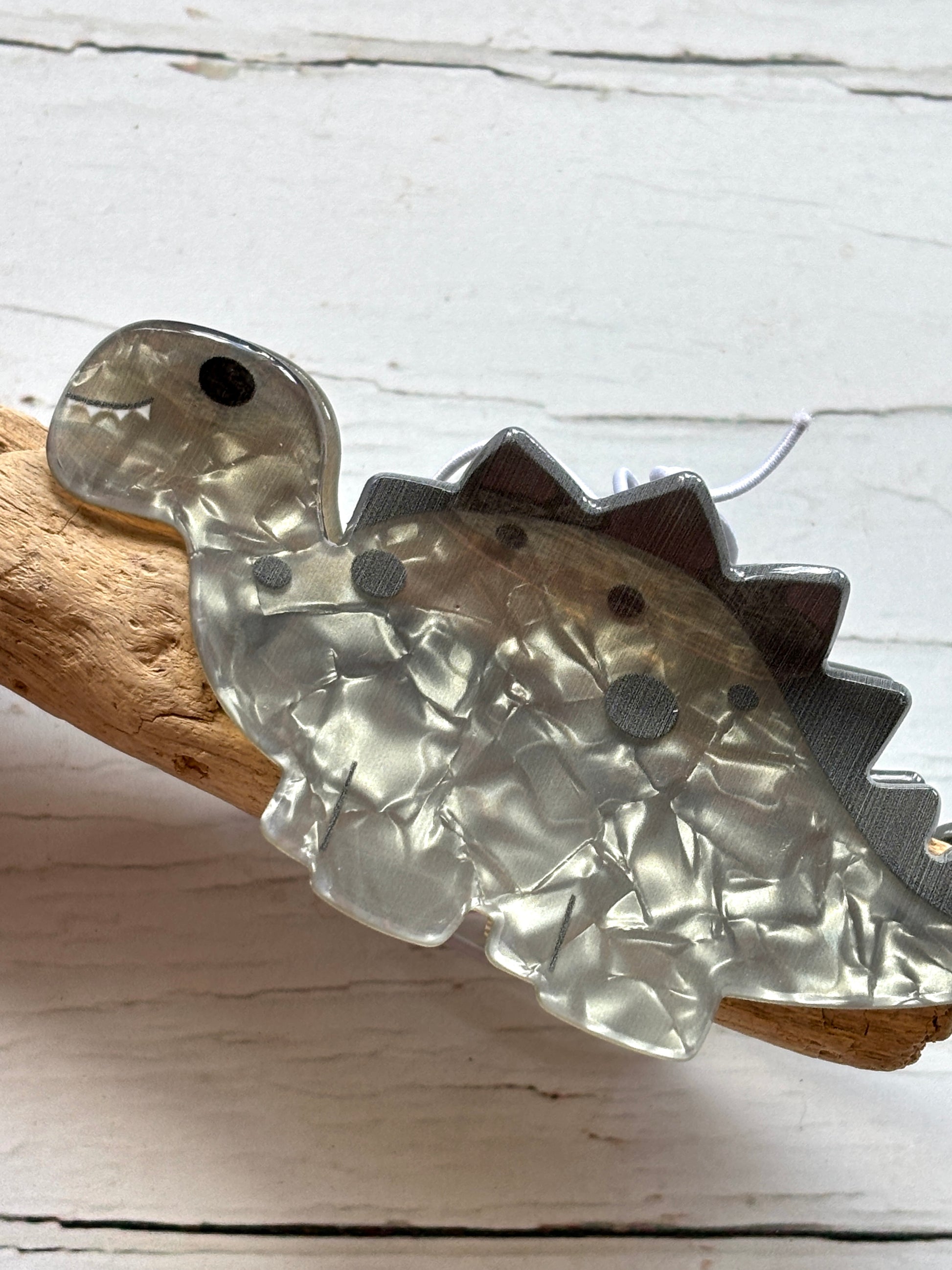 large marbled grey acrylic dinosaur hair claw clip funky novelty hair accessory or cute statement hair decor resting on driftwood