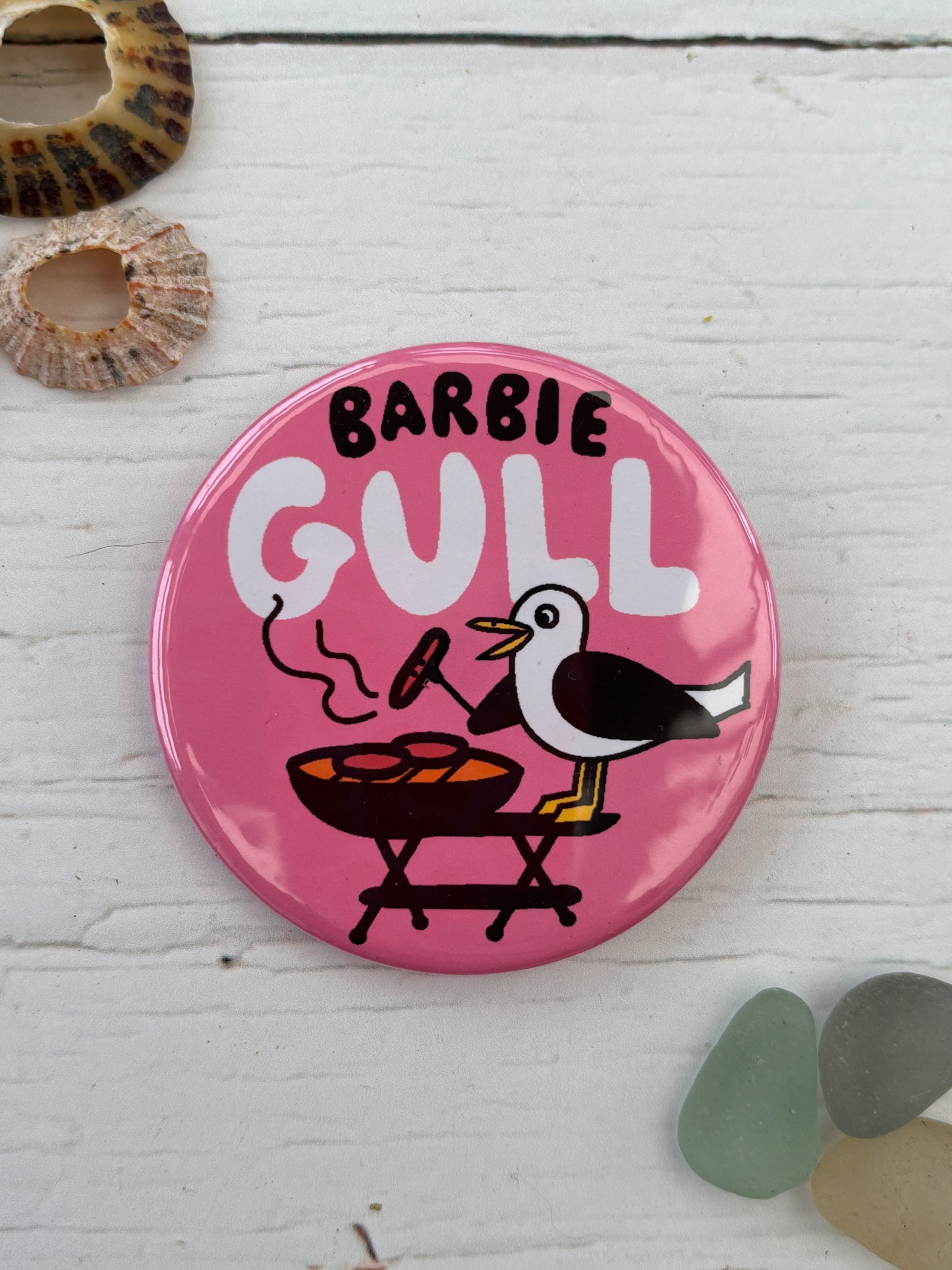 pink seagull badge with the text 'Barbie Gull' showing a bird cooking on a BBQ a funny novelty pin and coastal gift for beach lovers