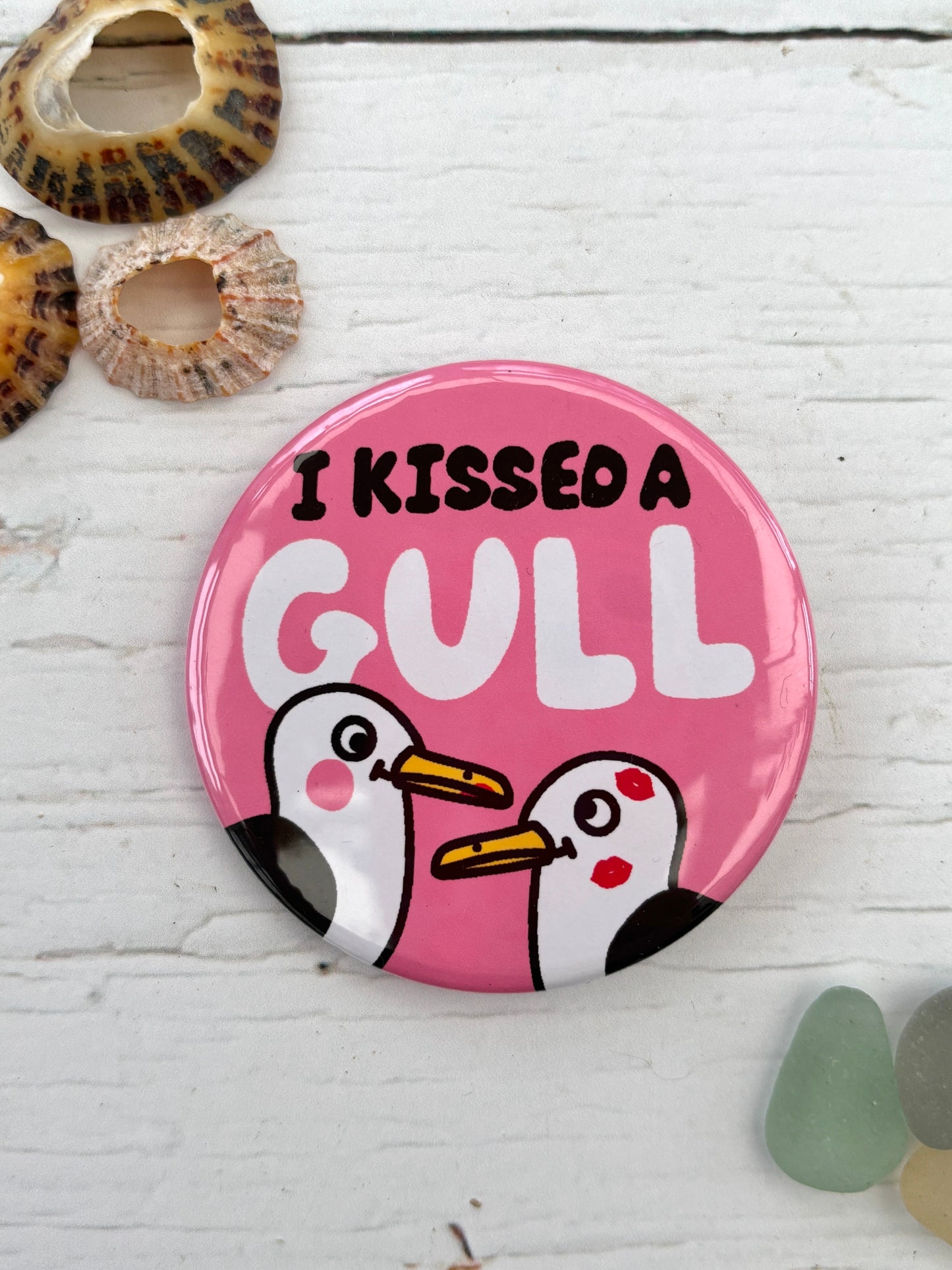 humorous pink badge featuring two seagulls and the text 'I Kissed A Gull' funny nautical accessory and a great coastal souvenir