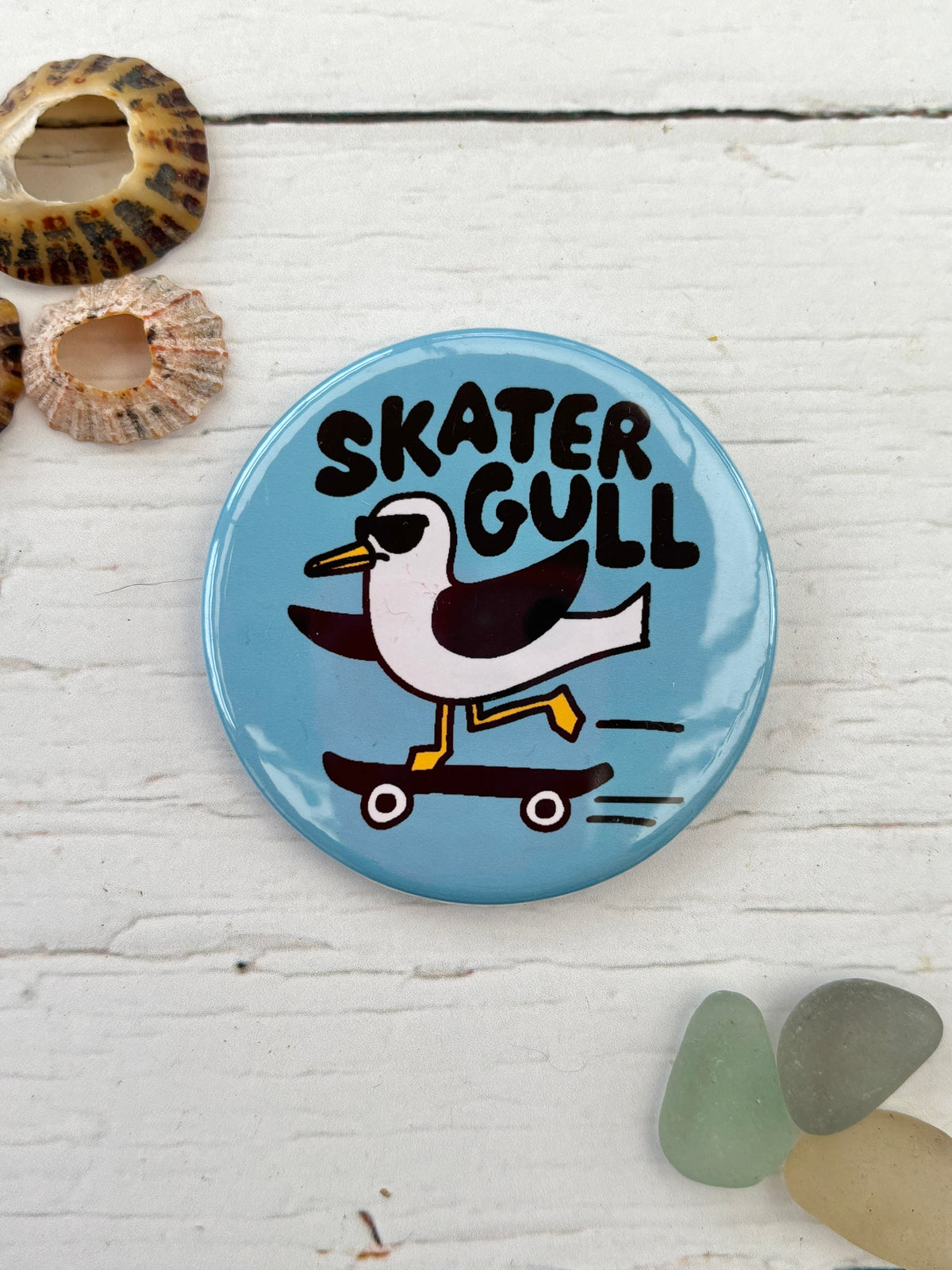light blue 'Skater Gull' badge featuring a seagull on a skateboard funky novelty pin and nautical accessory for a coastal look