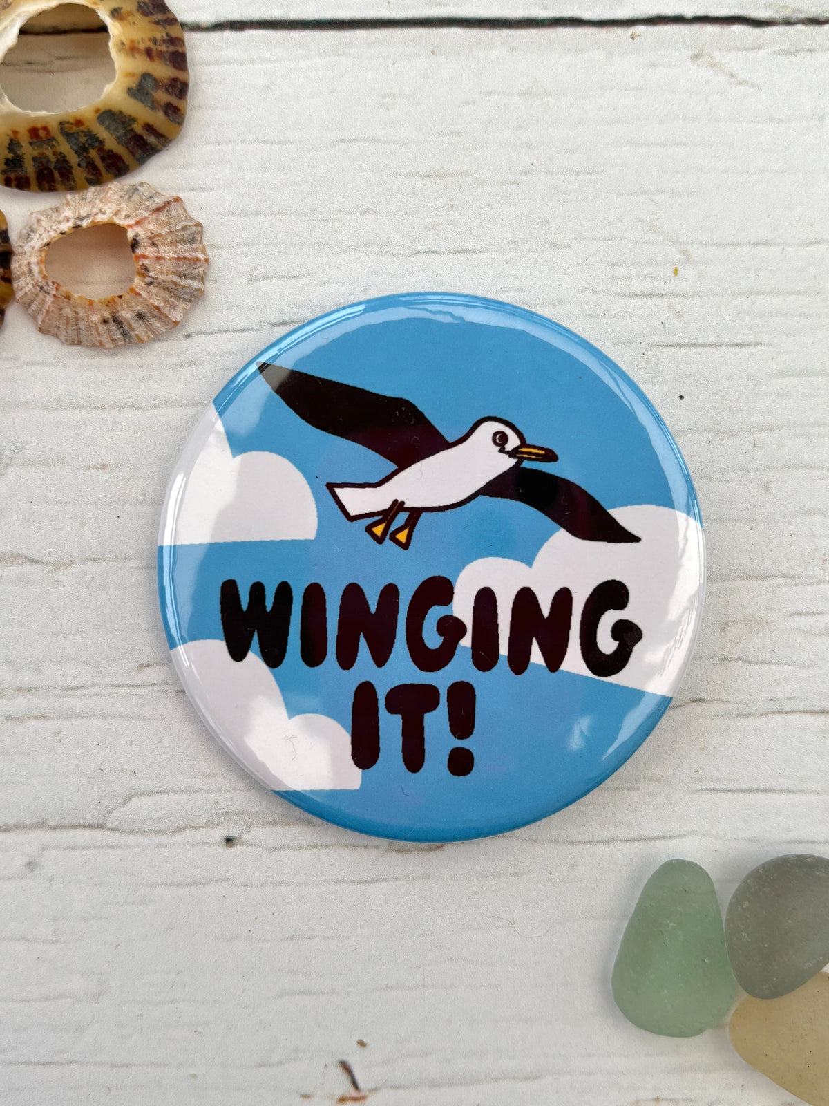 blue seagull badge with the text 'Winging It!' and clouds a funny novelty pin and nautical accessory great coastal gift for friends