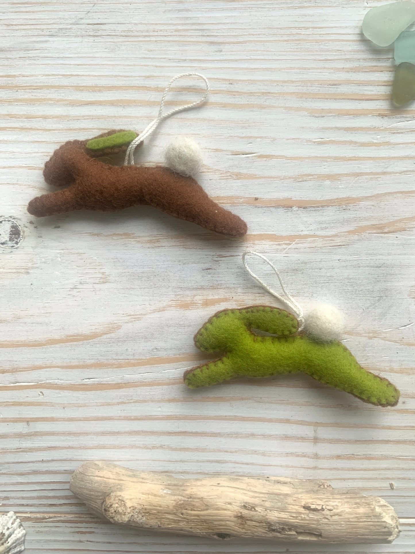 two handmade brown and green felt easter bunny decorations in a leaping position spring rabbit ornaments with fluffy pom-pom tails easter decor gift